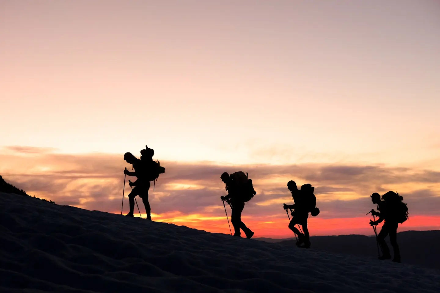 Silhouettes of four backpackers hiking up a hill at sunrise