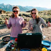 two women cooking dinner at camp wearing Solstice Sun Hoodies