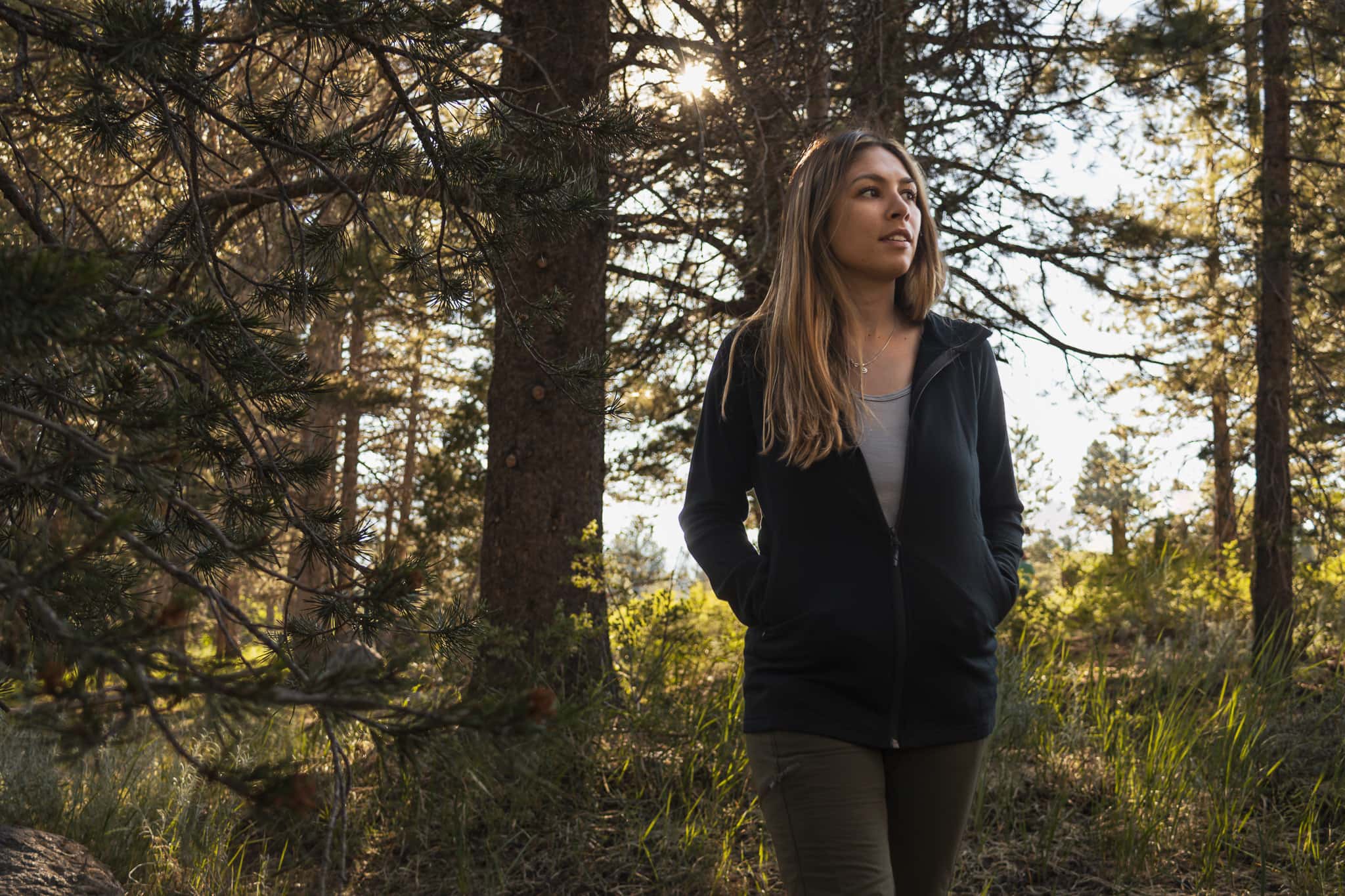 a woman stands in a forest in Mammoth Lakes wearing a Ridge Hyde Hoodie and Ridge Cami Tank