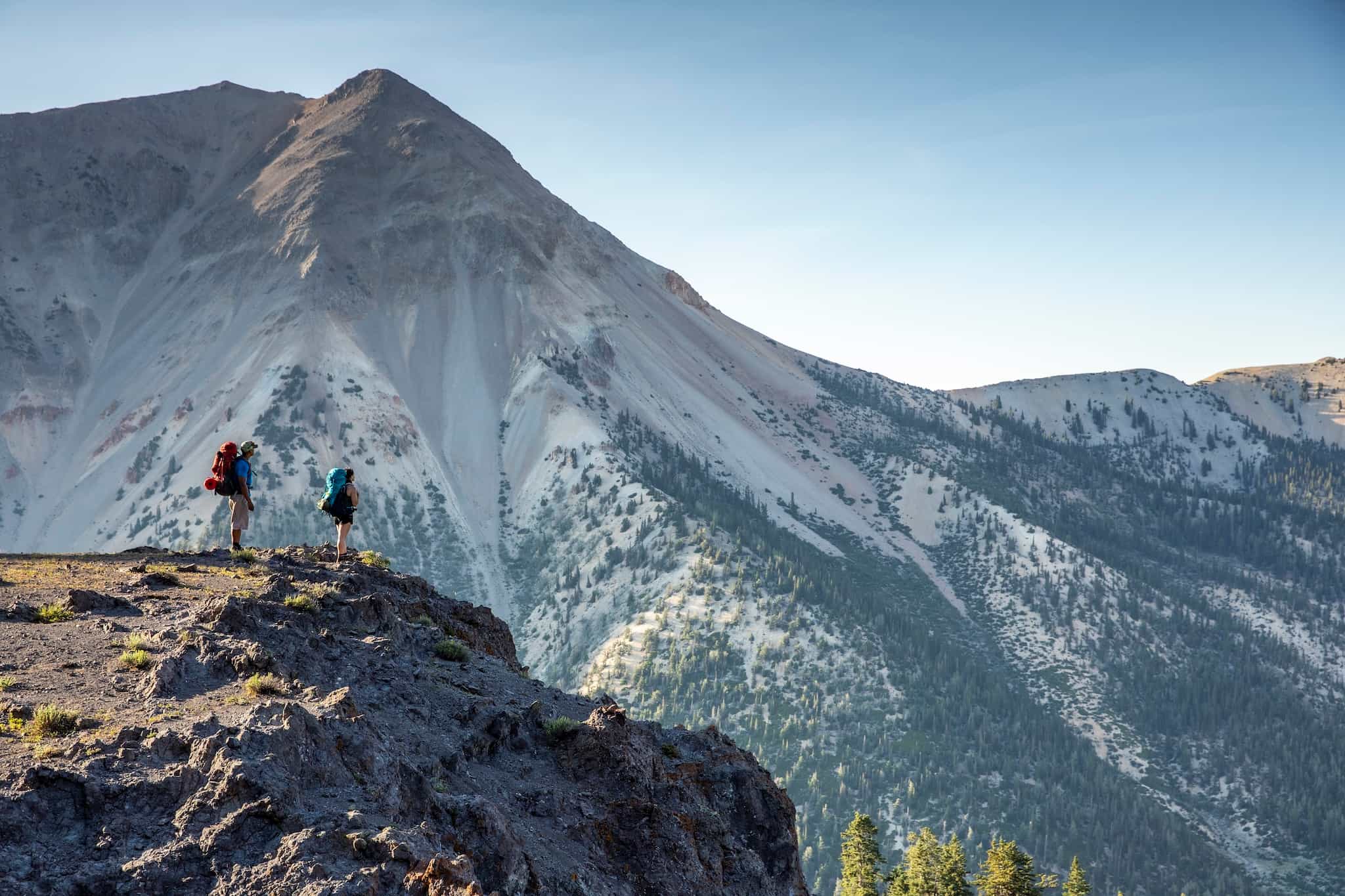 two backpackers stand beneath a large mountain