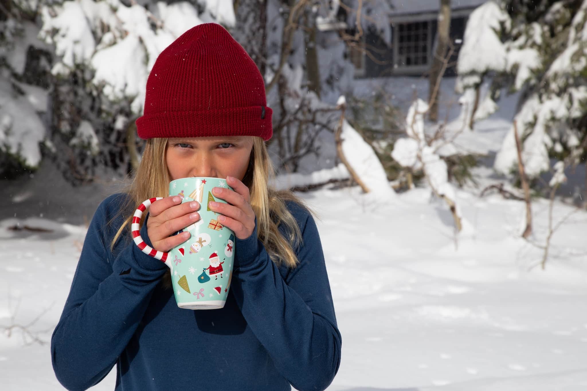 a kid drinks hot chocolate from a holiday mug wearing a Ridge beanie and Ridge kids' base layers