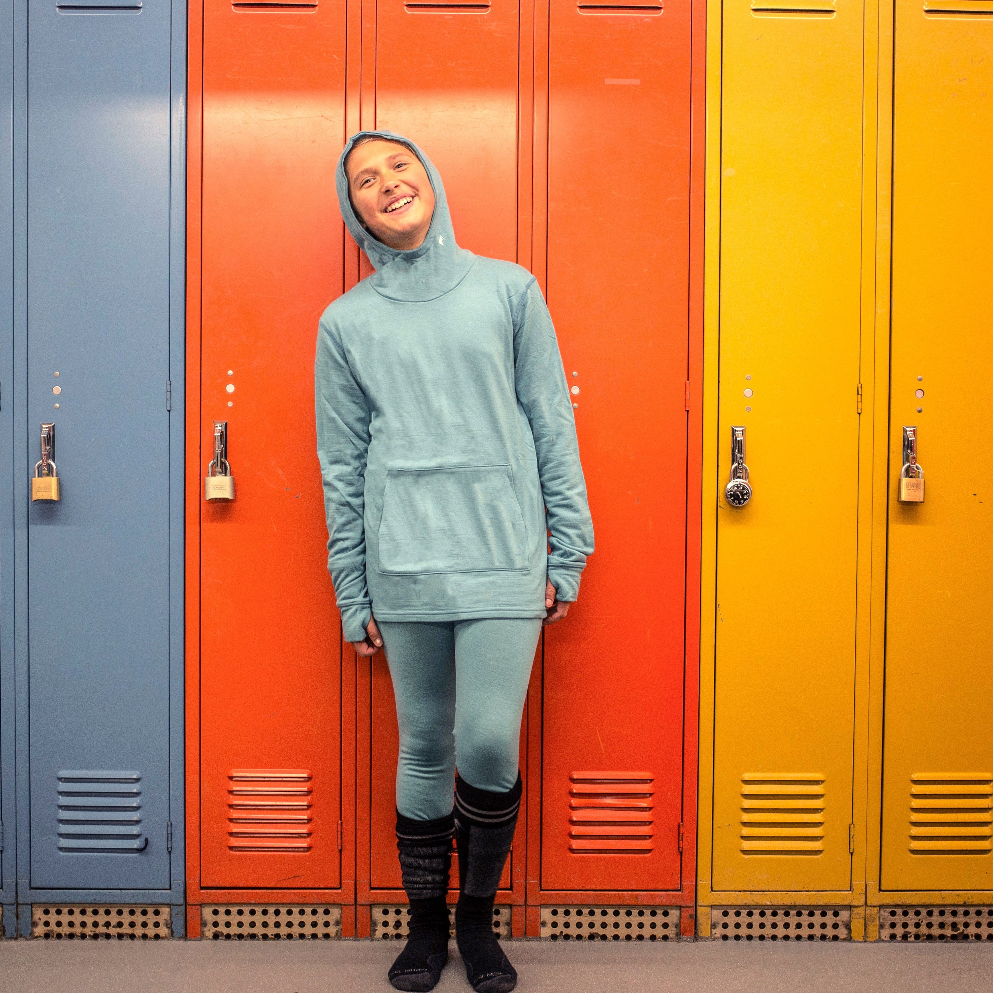 a girl wearing a Ridge Kids' Hyde Merino Hoodie and base layers in a ski locker room