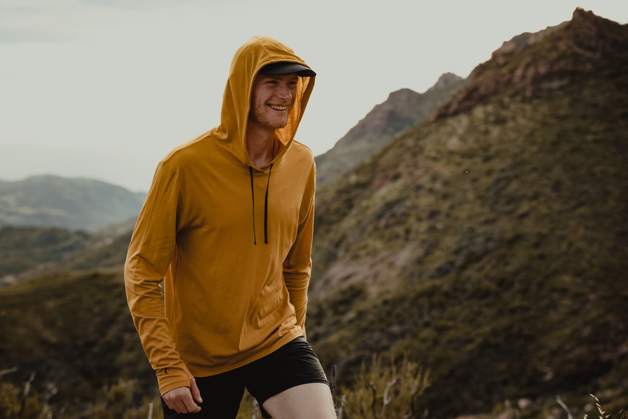 a trail runner smiles wearing a Ridge Merino solstice sun hoodie
