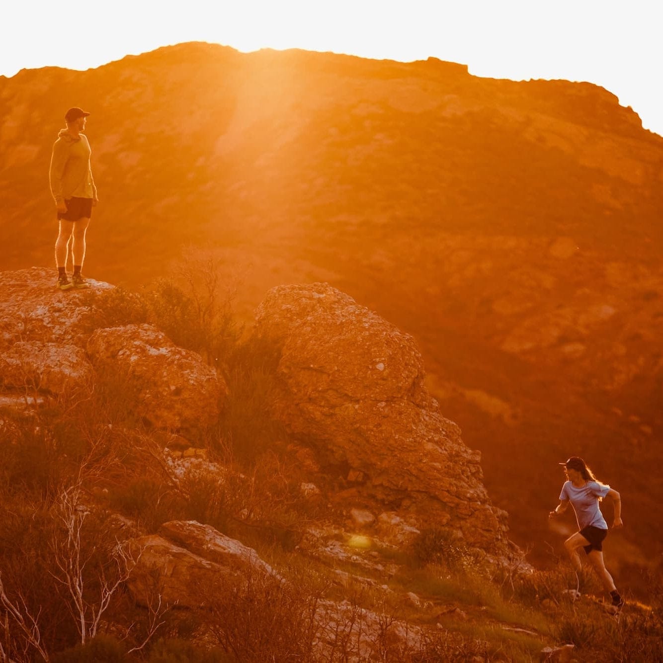 a woman runs up a hill at sunset toward a man wearing a Ridge Sun Hoodie