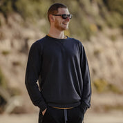 A man smiles wearing sunglasses and the Ridge Natural Tencel Crew Sweatshirt on a beach