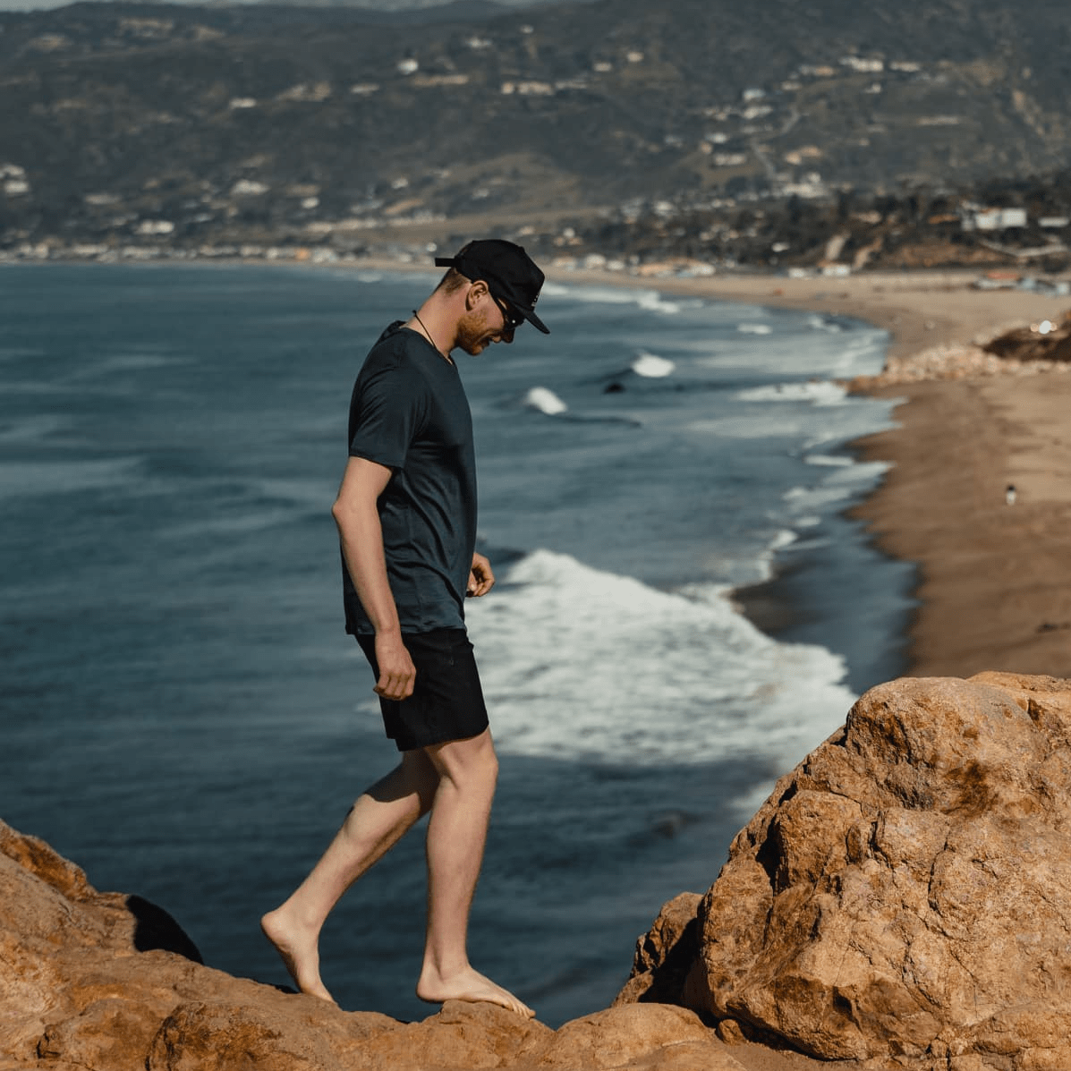a man walks on a beach wearing a Ridge Merino Journey Tee