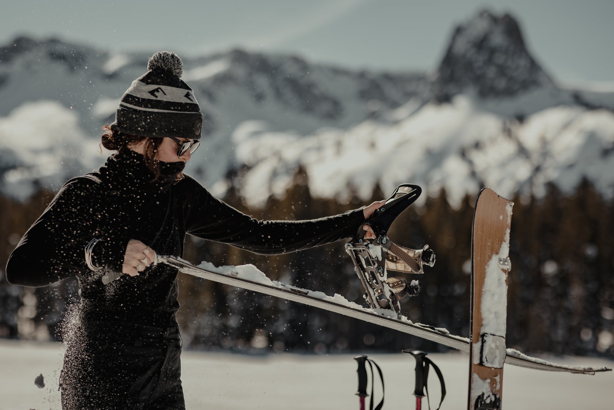 a woman adjusts her backcountry splitboard on a touring day wearing Ridge Merino layers