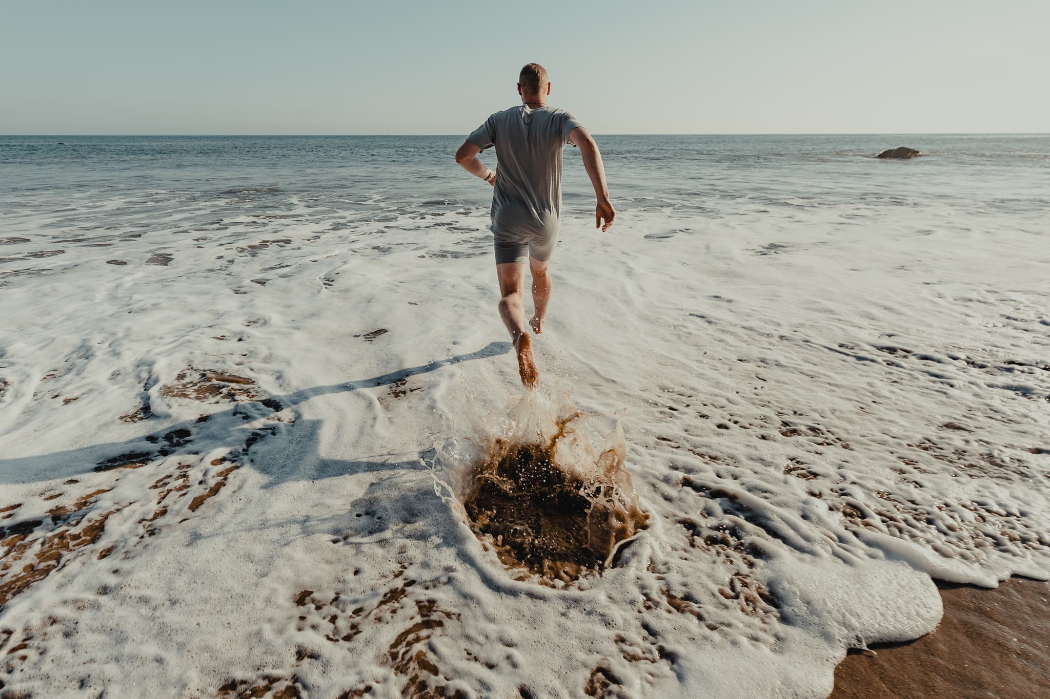 a man wearing Ridge Merino boxers and a Ridge Merino tee runs into the ocean on a sunny morning