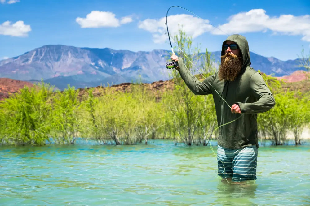 A fly fisherman casts in a stream on a bright summer day