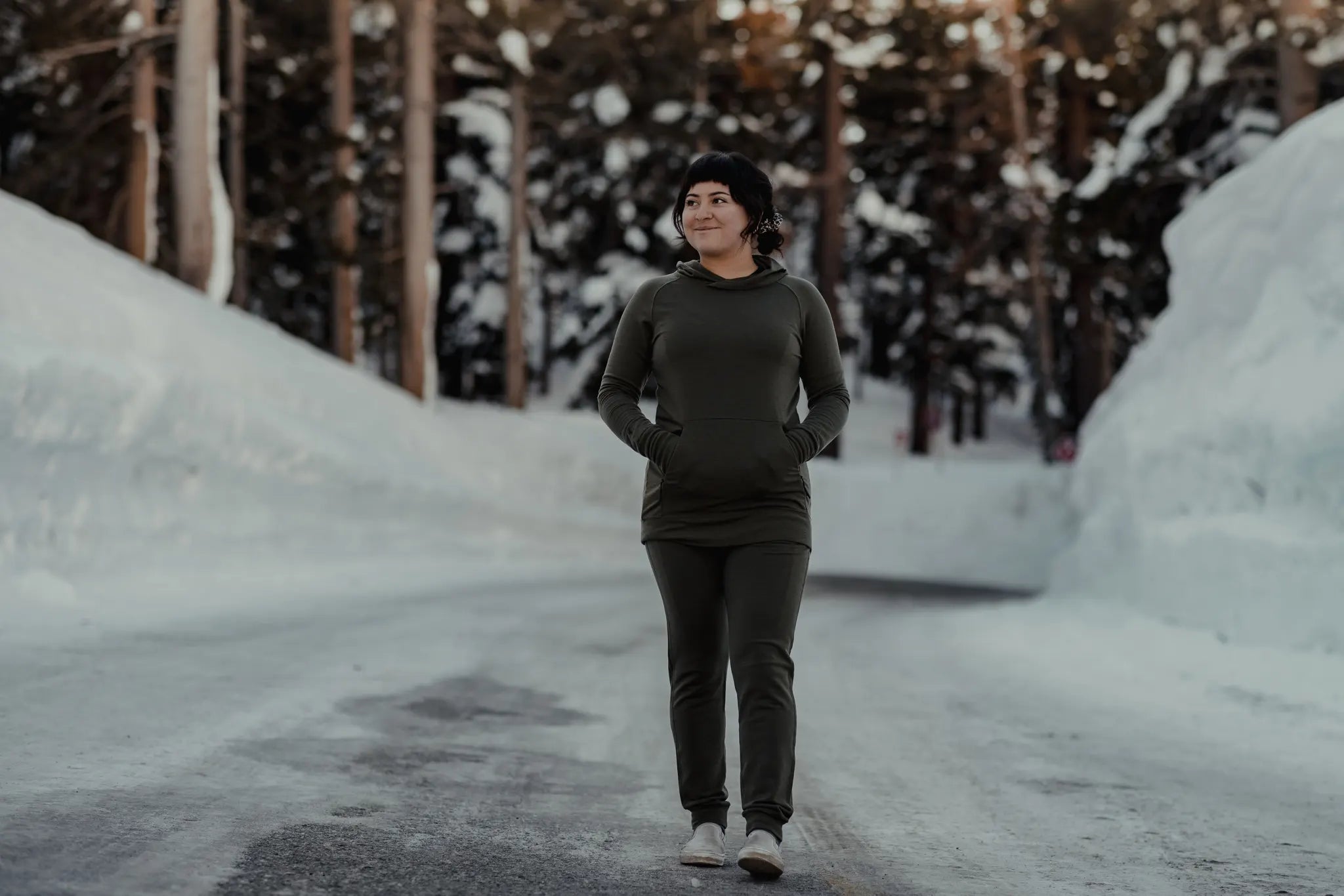 a woman stands on a snowy road wearing Ridge Merino joggers and hoodie