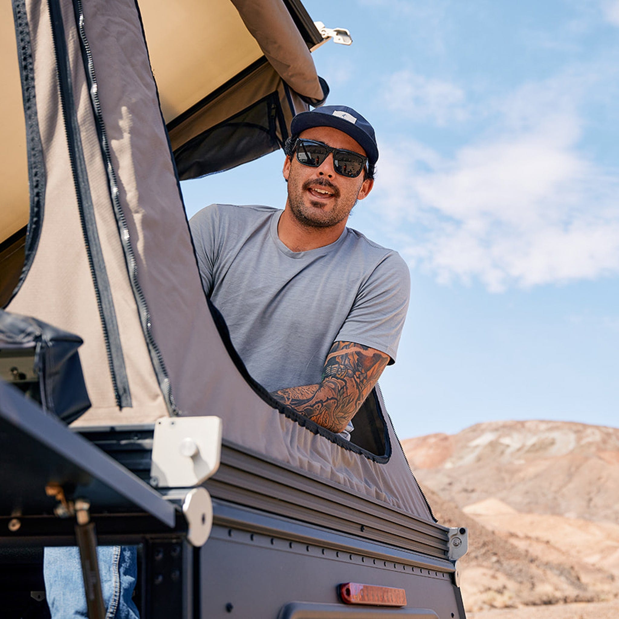 a man wearing the Journey T-Shirt leaning out of a rooftop tent on a camping trip