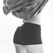 A woman lounging in Ridge Merino boy shorts and a flannel shirt