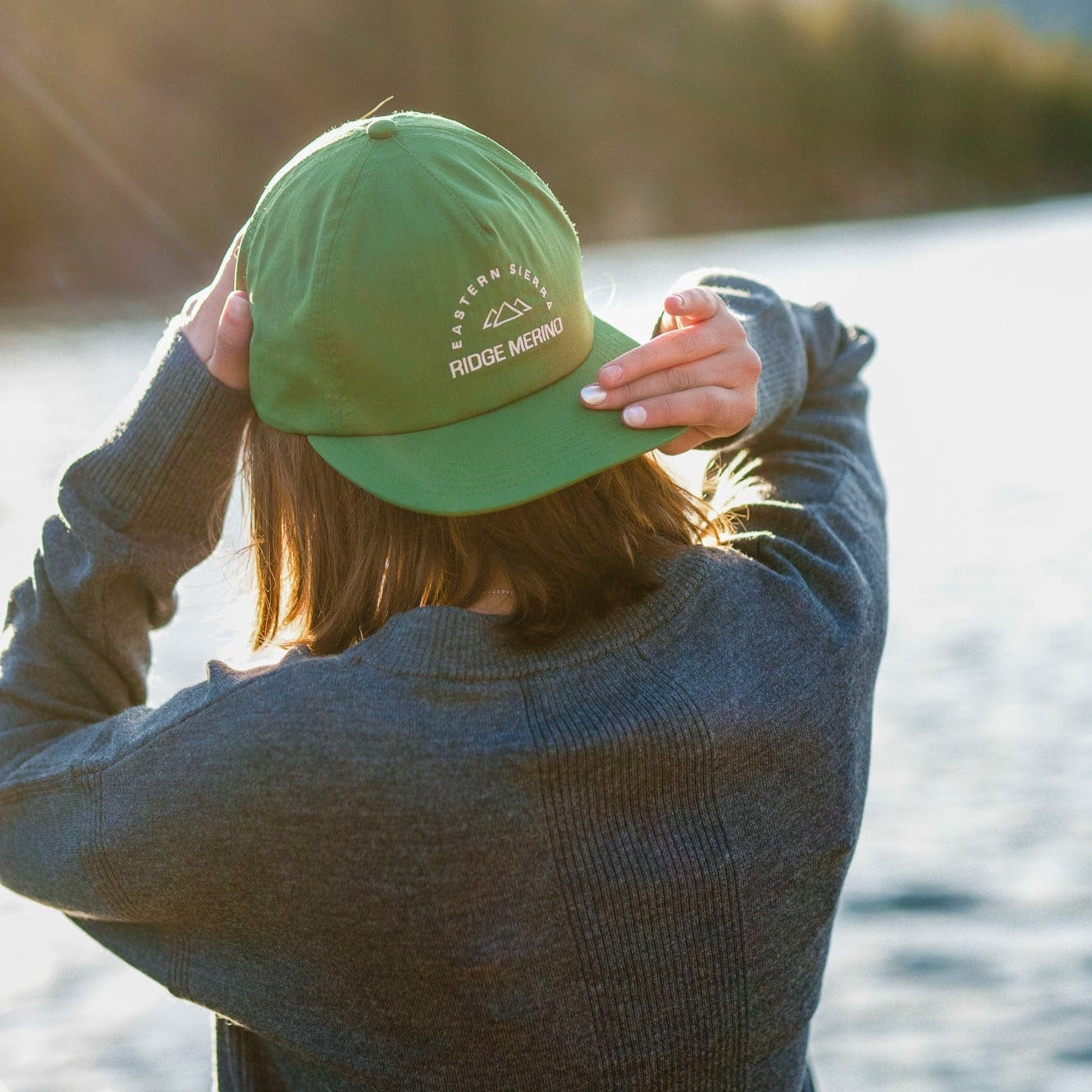 a woman putting on a Ridge Sherwin hat backwards on a summer day