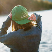 a woman putting on a Ridge Sherwin hat backwards on a summer day