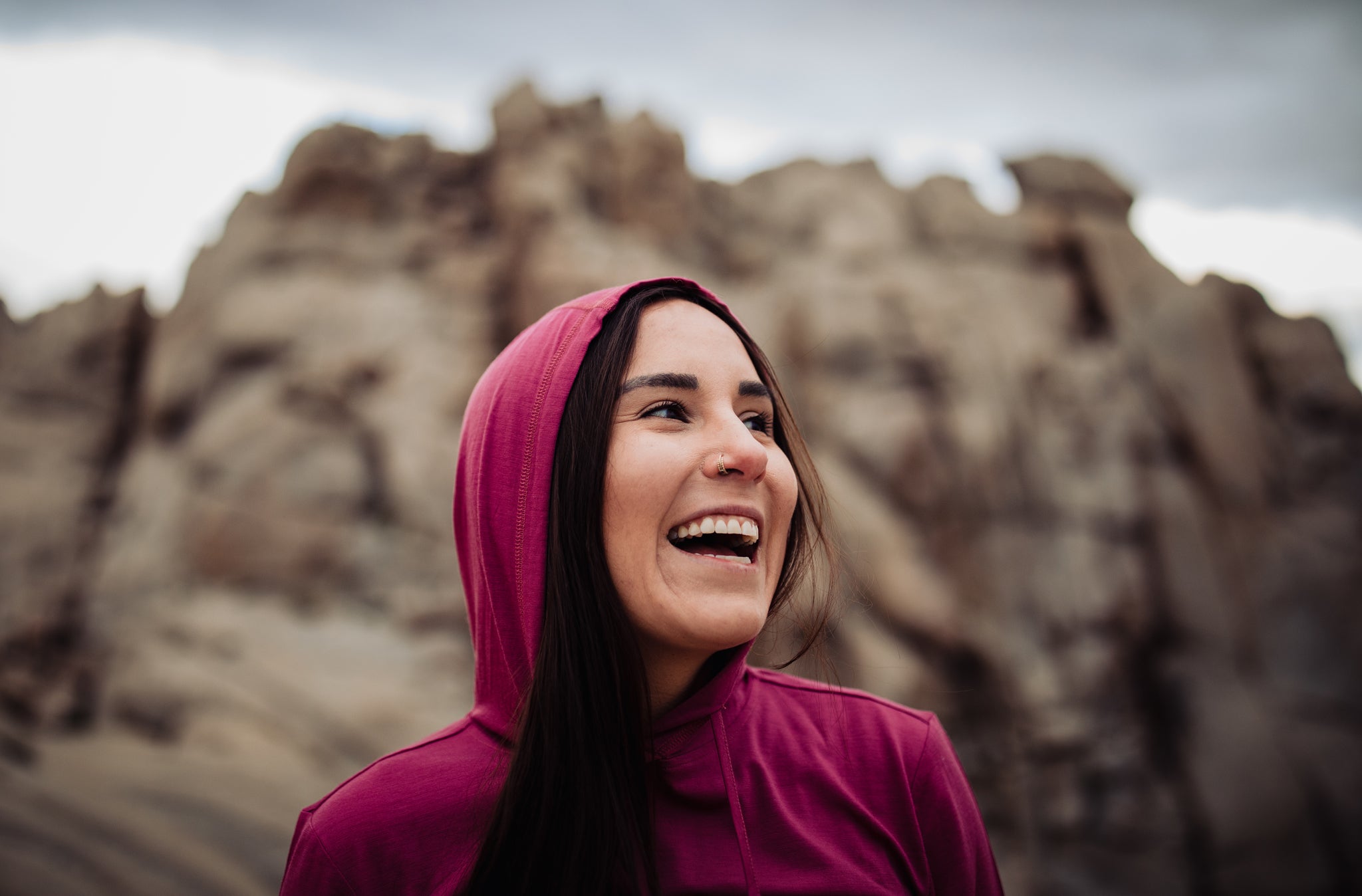 a woman smiles wearing a pink Solstice Sun Hoodie in the desert