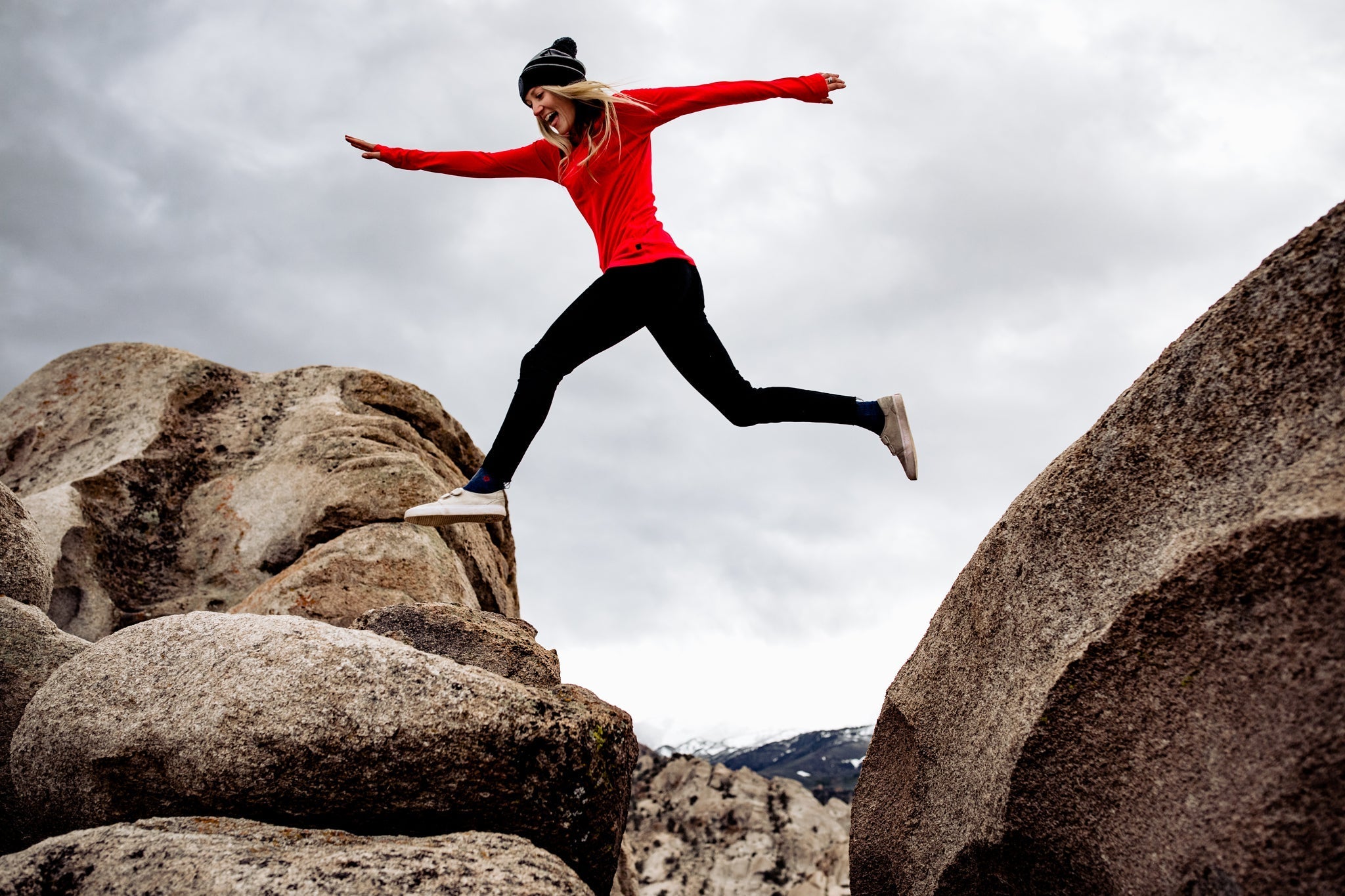 a woman jumps from one rock to another wearing a Ridge Merino shirt