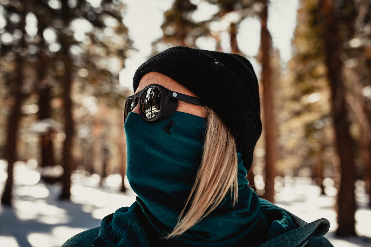 a woman wearing a Ridge Merino neck gaiter, beanie and sunglasses in the forest