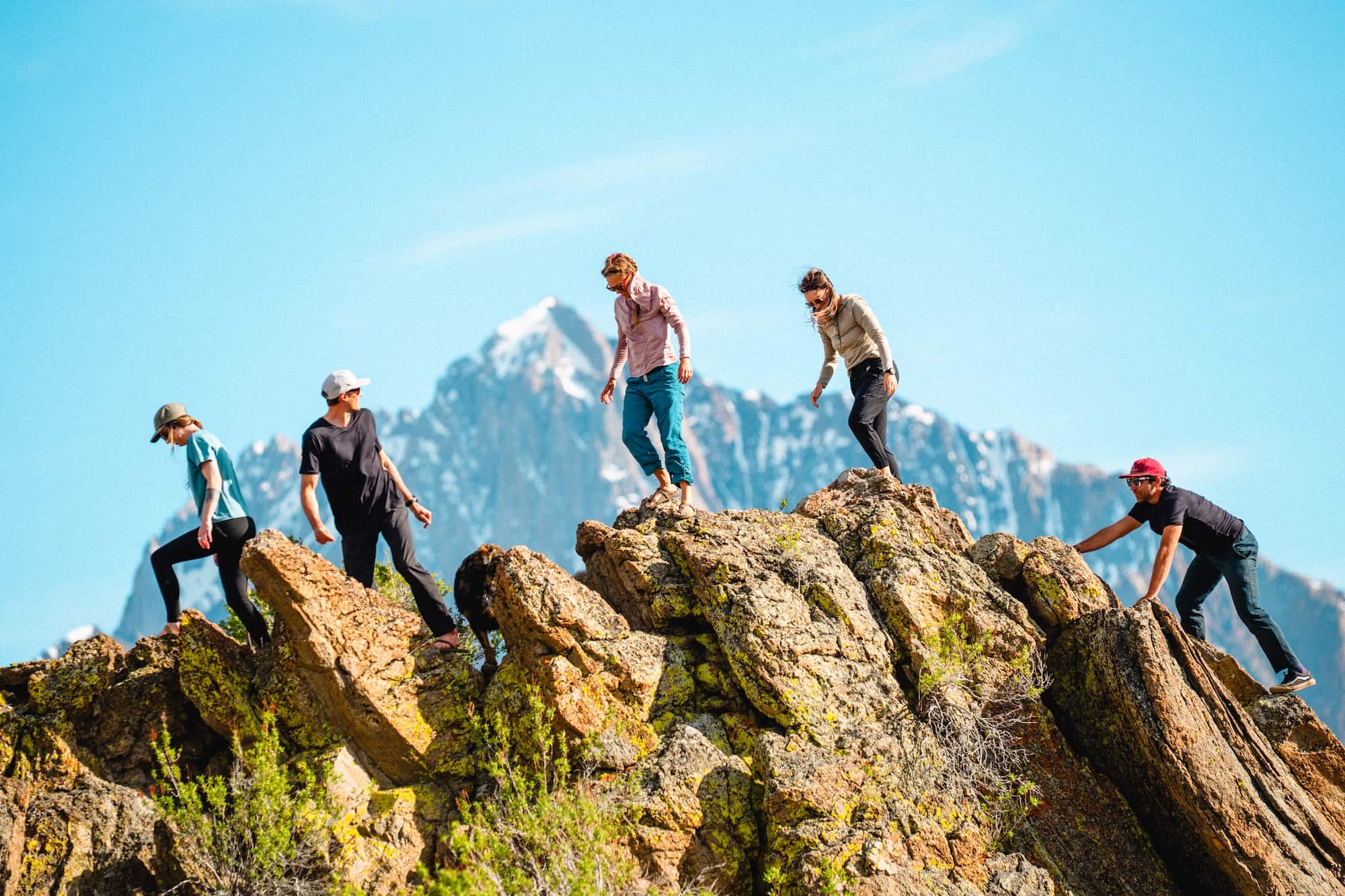 a group of friends scrambling on a rock feature in the Mammoth Lakes area wearing Solstice Sun Hoodies and Ridge Merino Tees