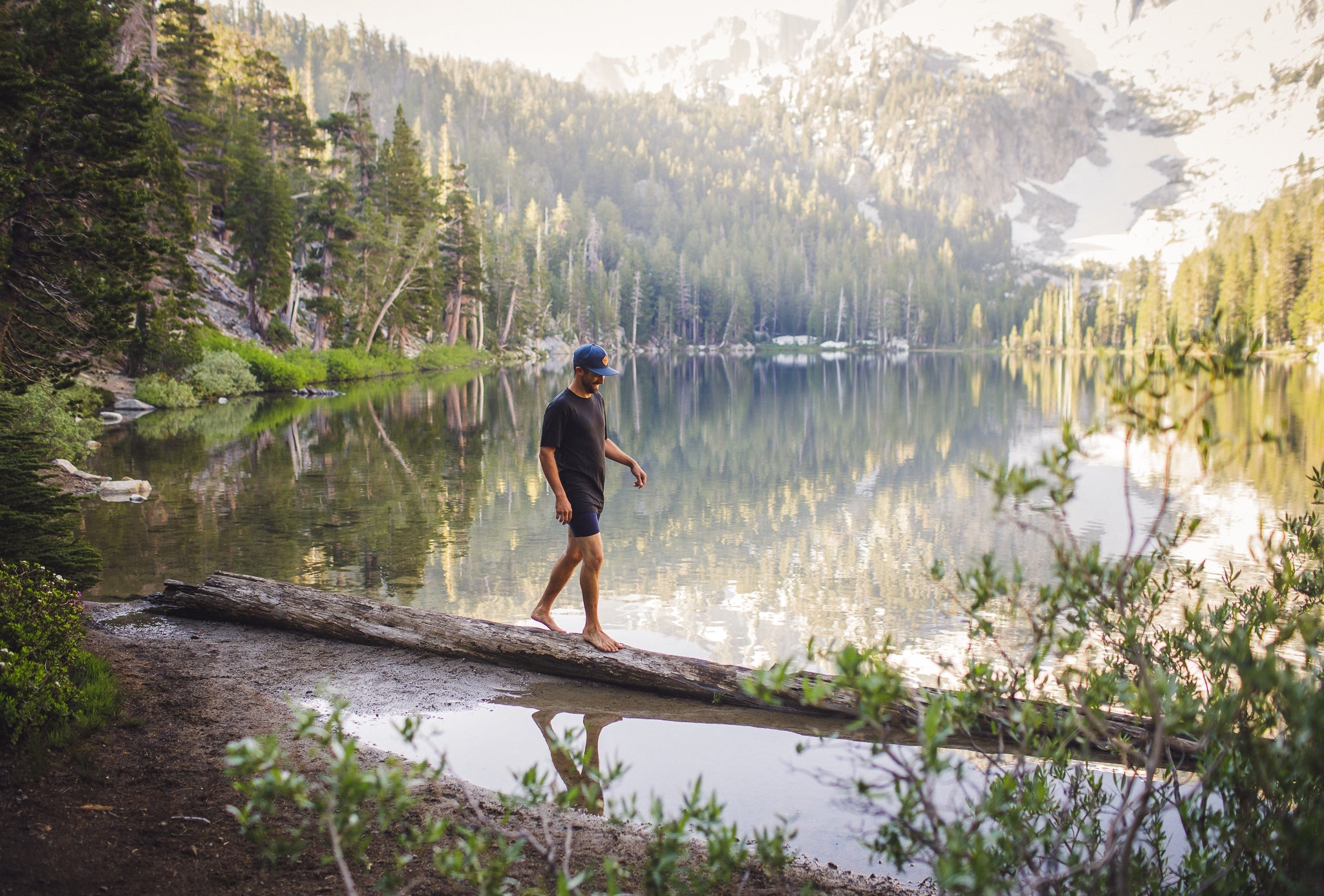 a man walks across a log in a backcountry lake wearing a Ridge t-shirt and Ridge Merino Boxer Briefs
