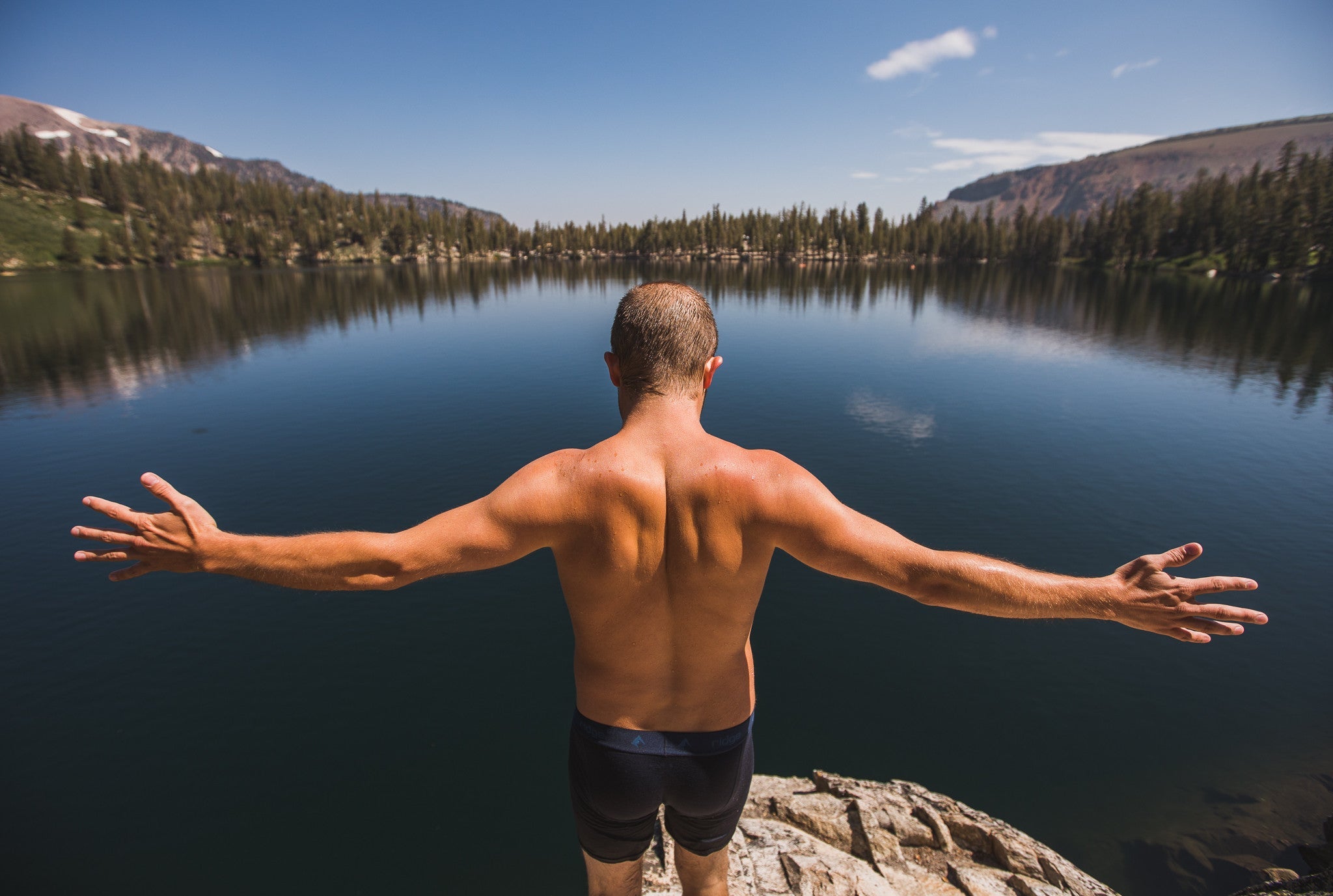 a man spreads his arms before diving into an alpine lake in his Ridge Merino underwear