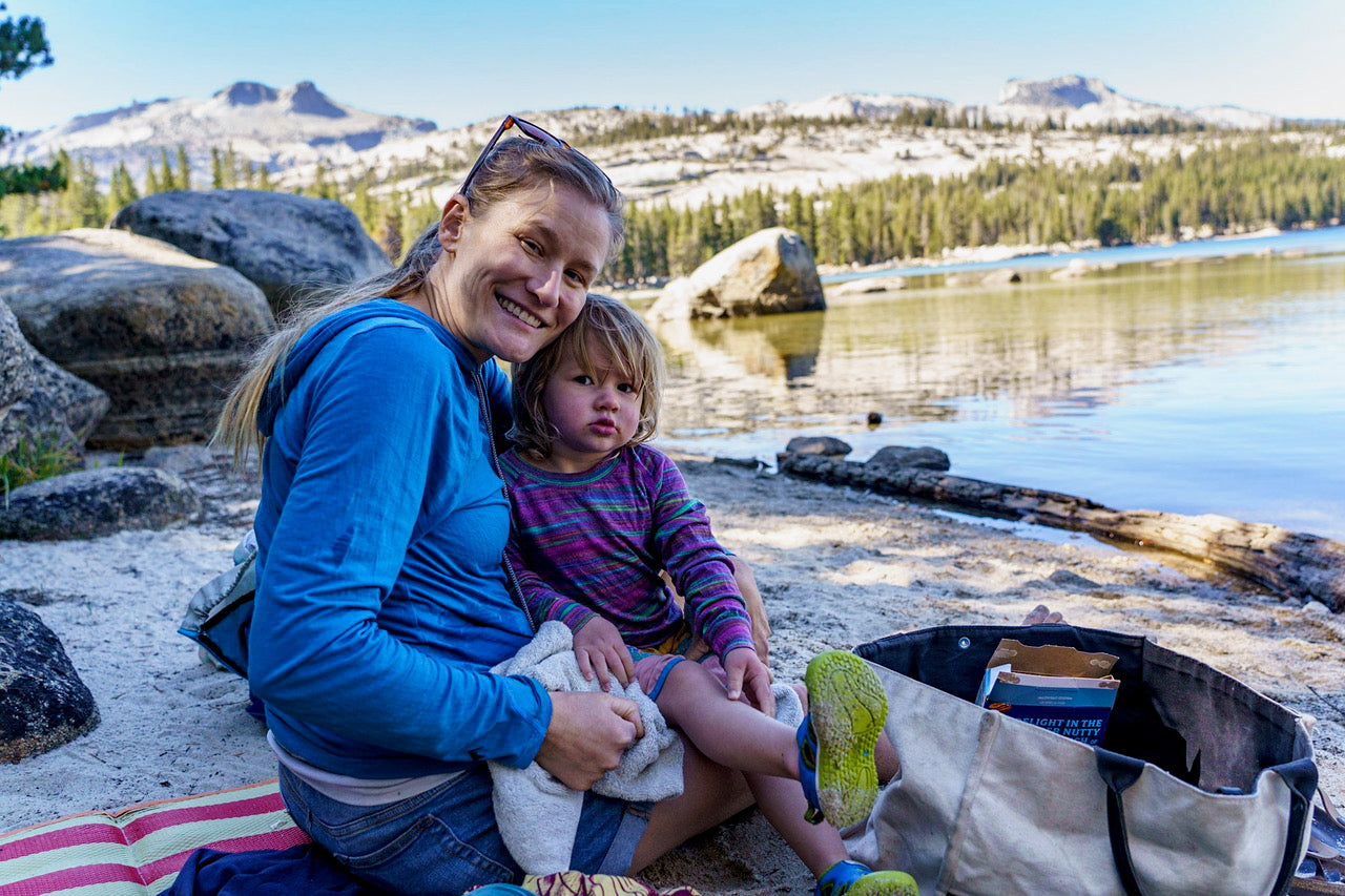 a woman smiles on a hike with her young daughter, both wearing Ridge layers