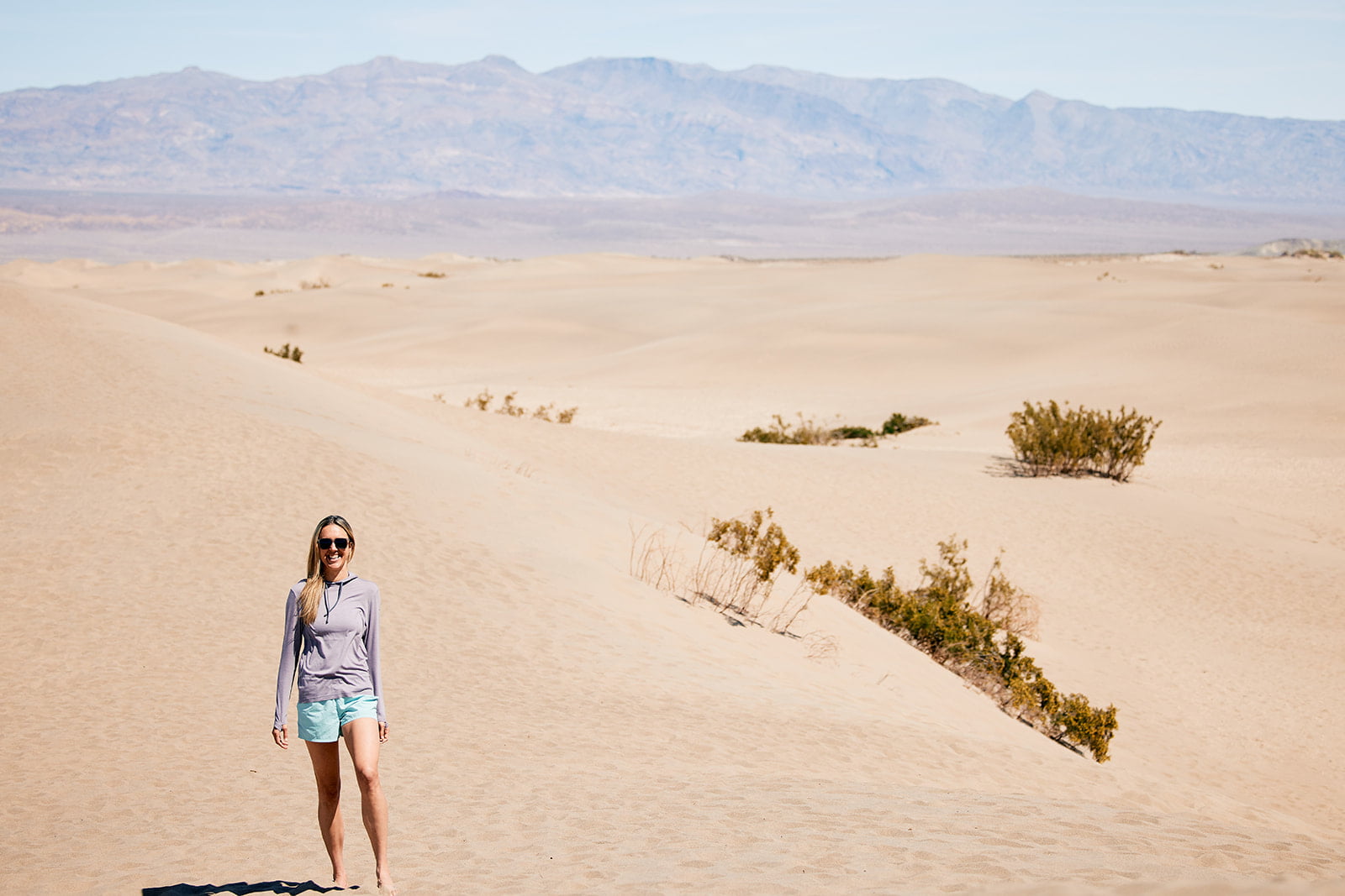 a woman hikes around sand dunes wearing a Ridge Merino Solstice Sun Hoodie