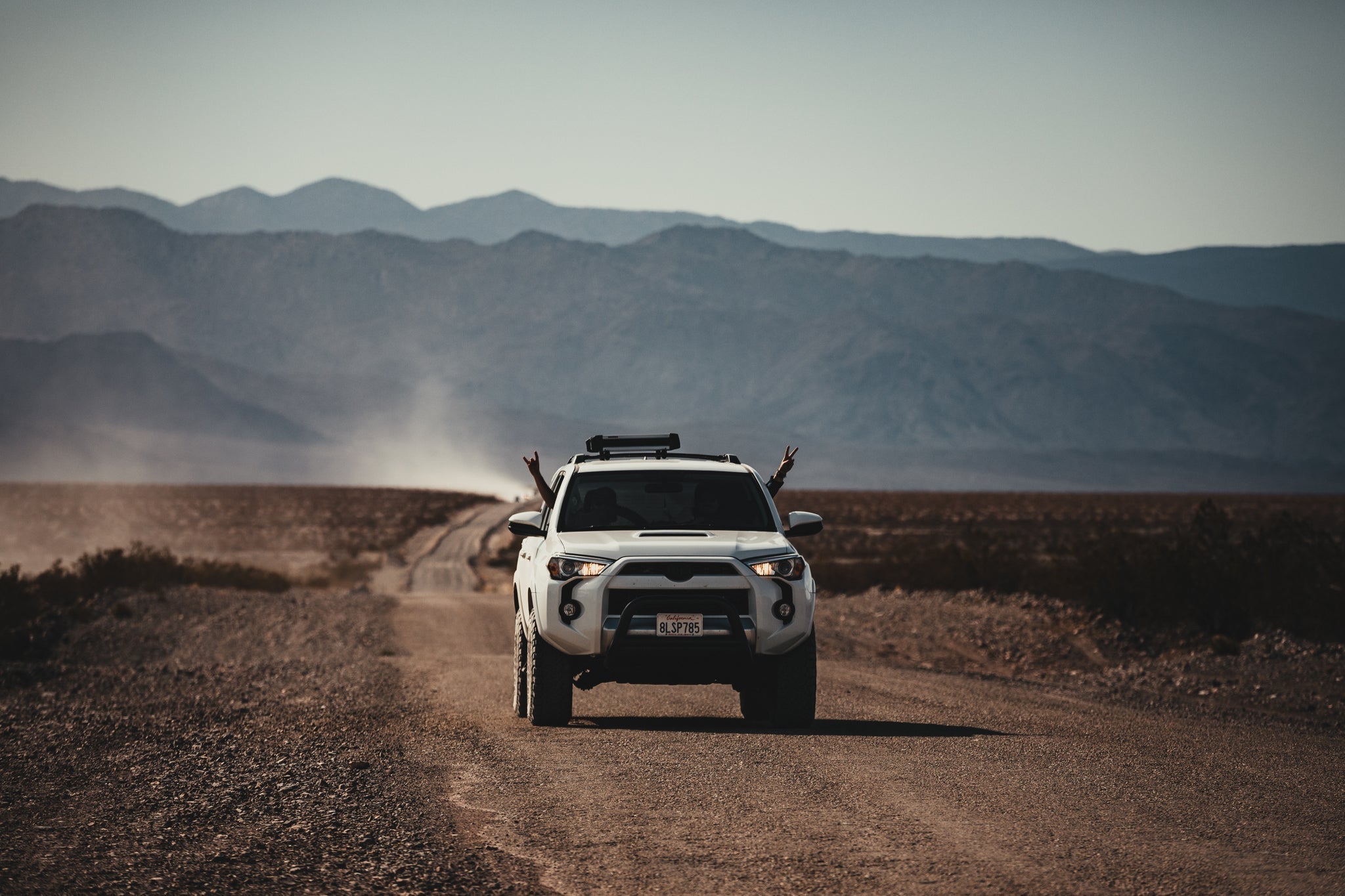 a white SUV driving on a dirt road with people putting their hands out the windows excitedly