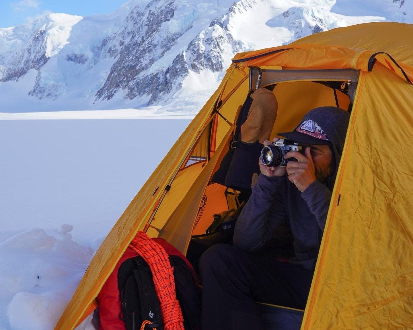 Nick Cahill photographs a scene from a yellow tent set up in snowy mountains