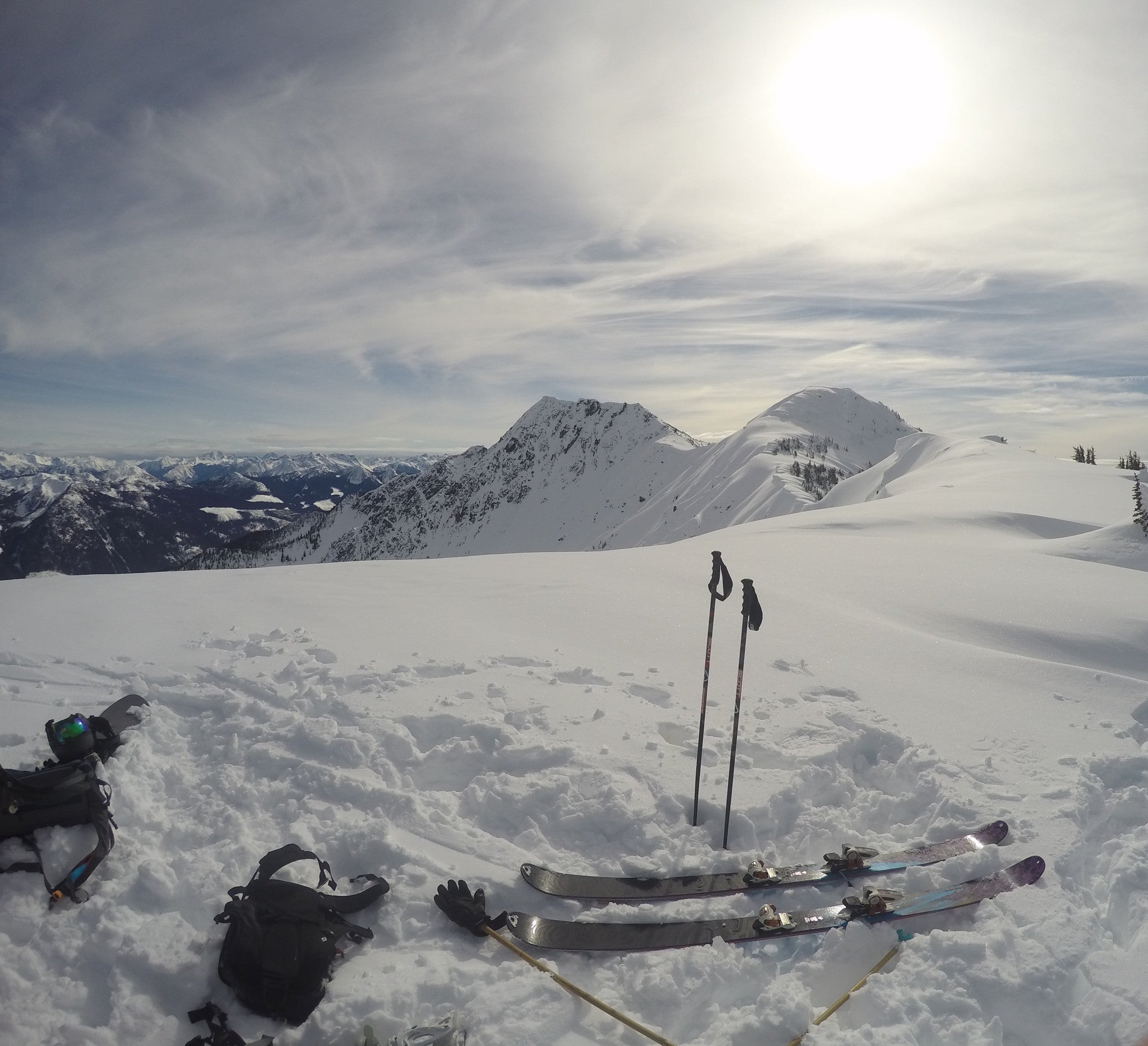 backcountry ski gear laid out at the top of a run on a snowy day