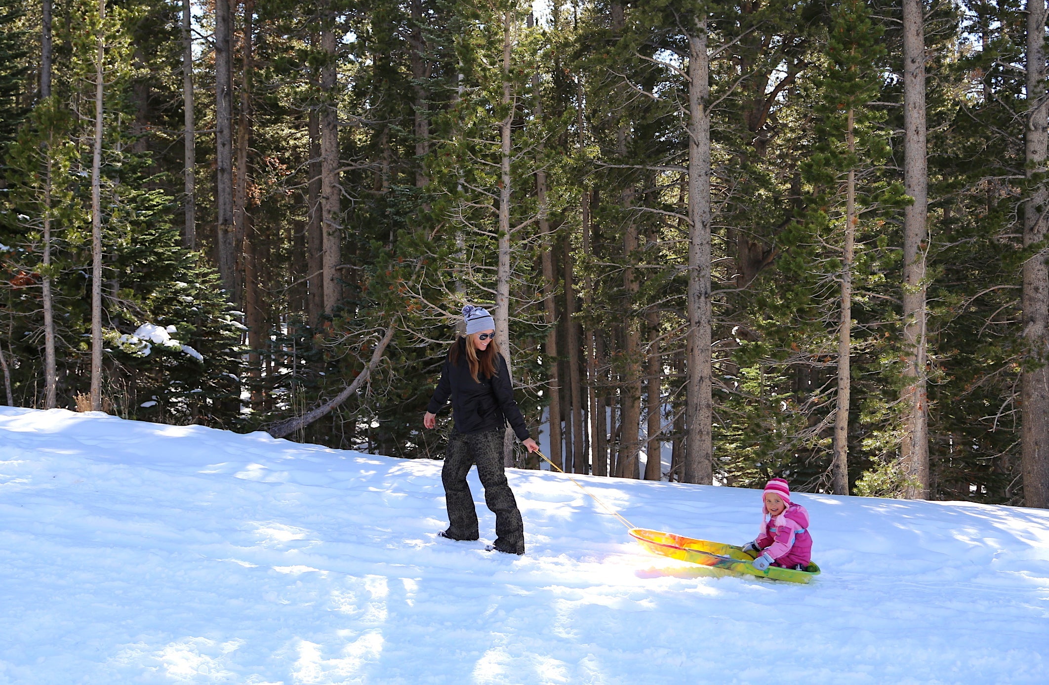 a mom pulling her child up a hill on a sled