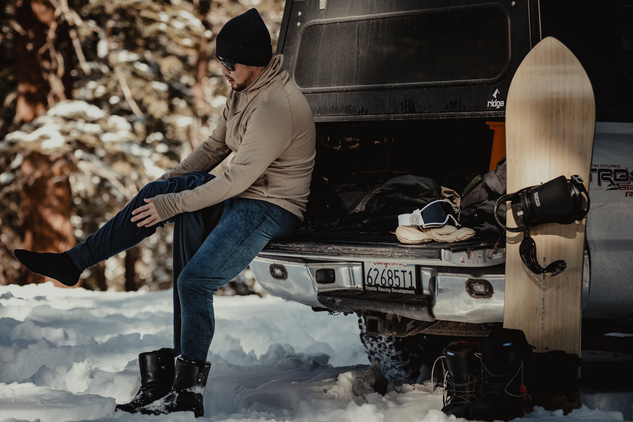 a man sits on the tailgate of his truck layering up for a splitboarding adventure