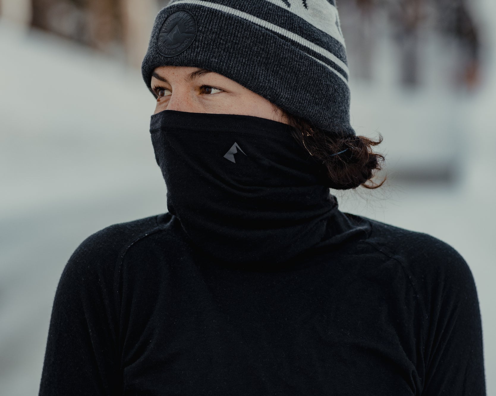 a woman wearing the Aspect Merino Wool High Neck Top and Ridge Logo Pom Merino Wool Beanie