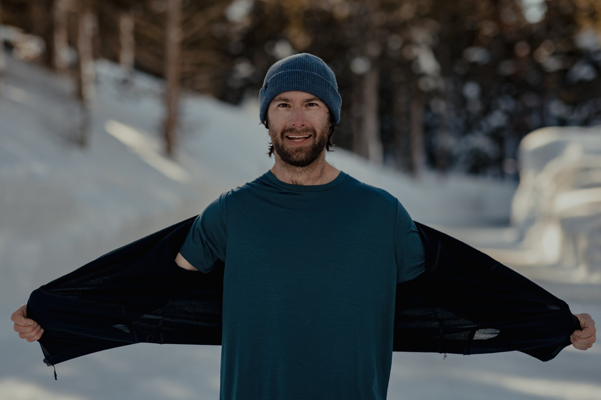 a man shows off his Ridge t-shirt under his Ridge base layer on a snowy road