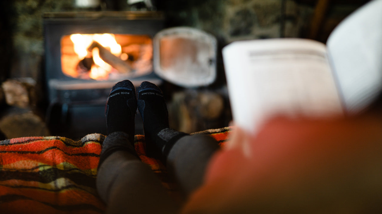 a person reading by the fire wearing cozy Ridge Merino Banked Socks