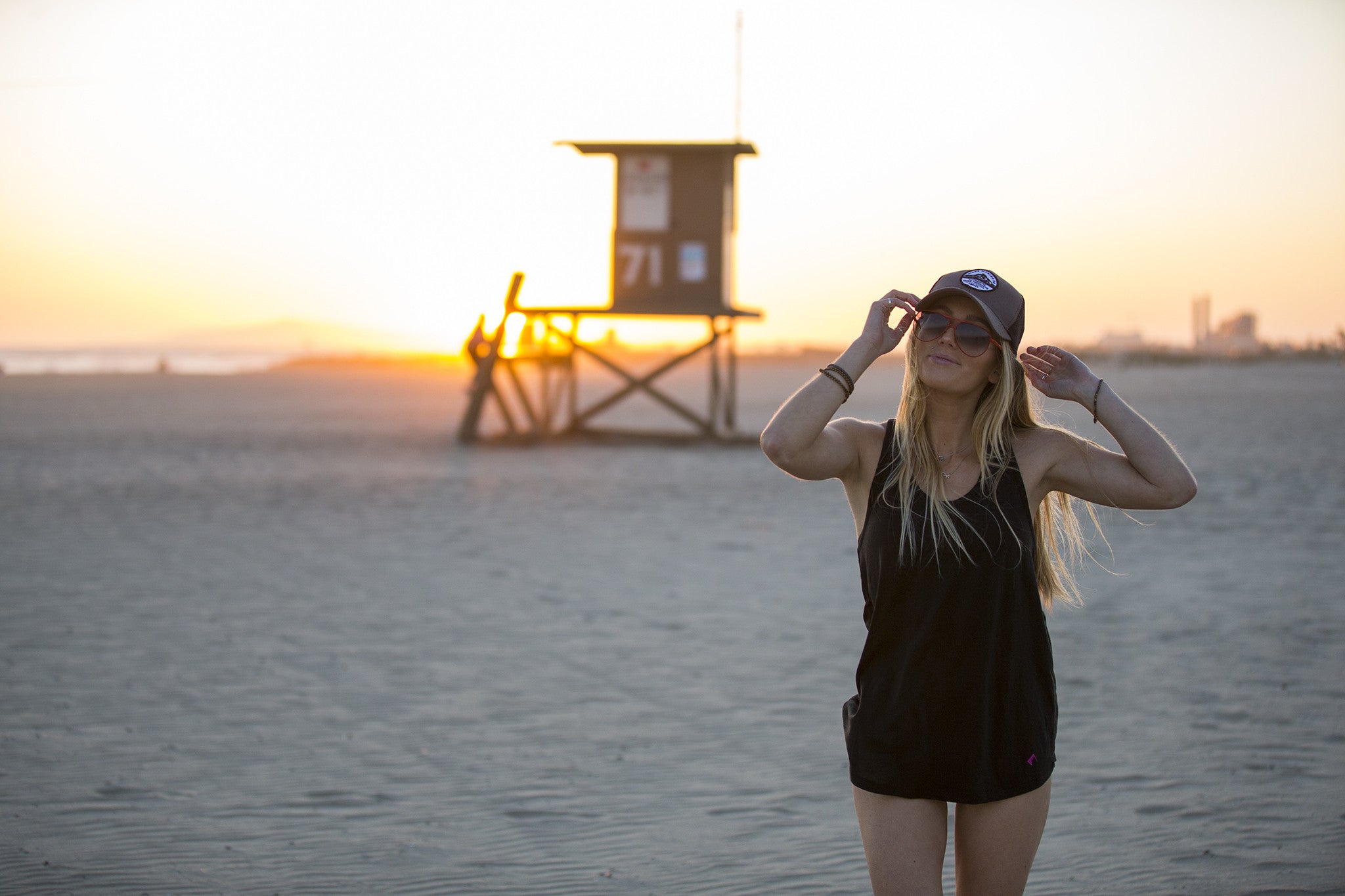 a woman wearing a Ridge Merino hat on the beach with a lifeguard stand behind her
