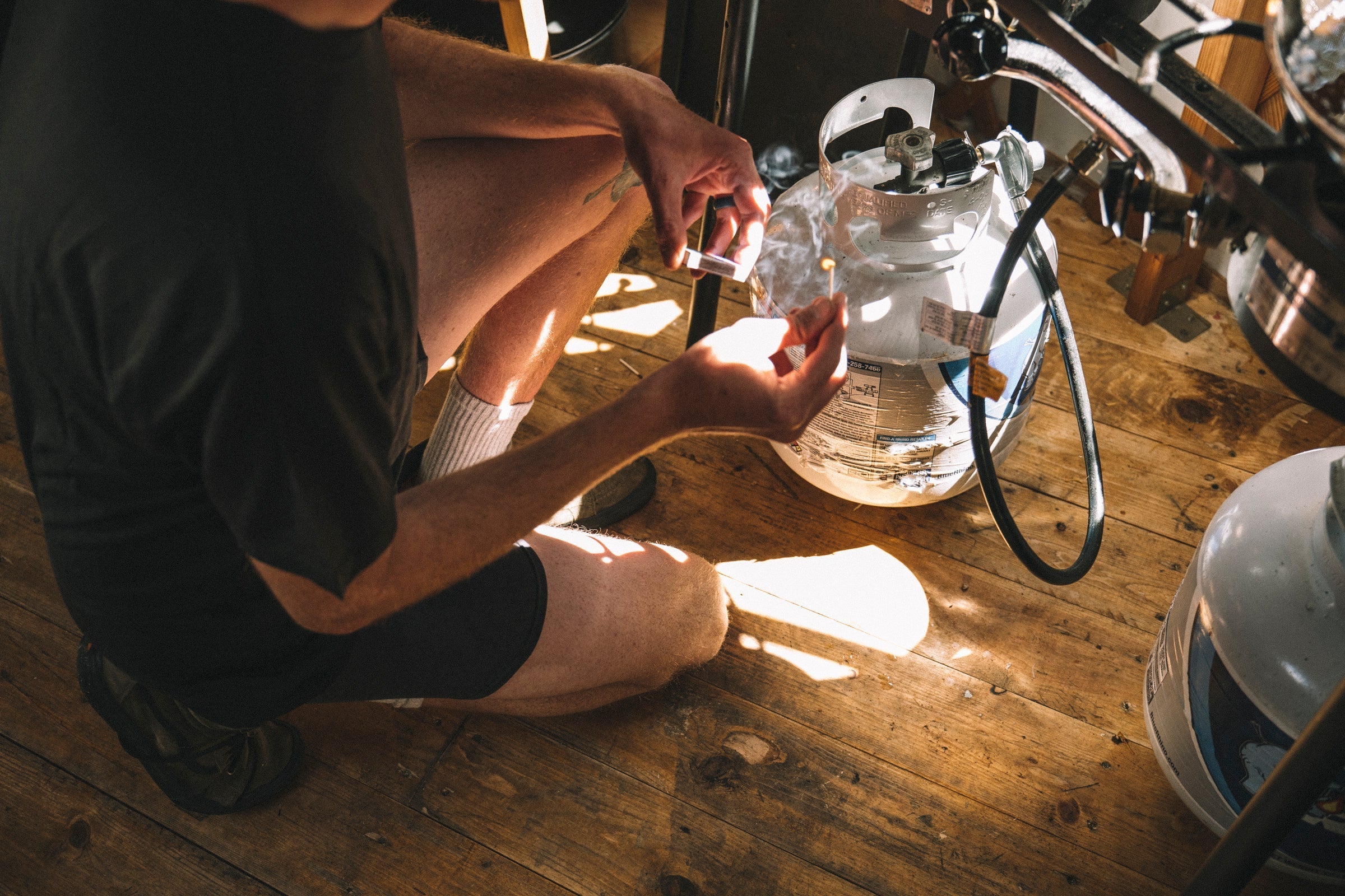 a man lights a camp stove in a backcountry ski yurt in Ridge Merino underwear and a Ridge Journey Tee
