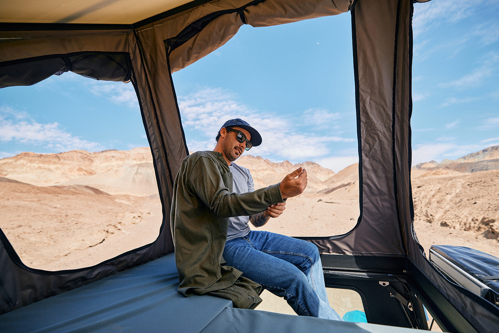 a man putting on an overshirt in the desert while in a rooftop tent
