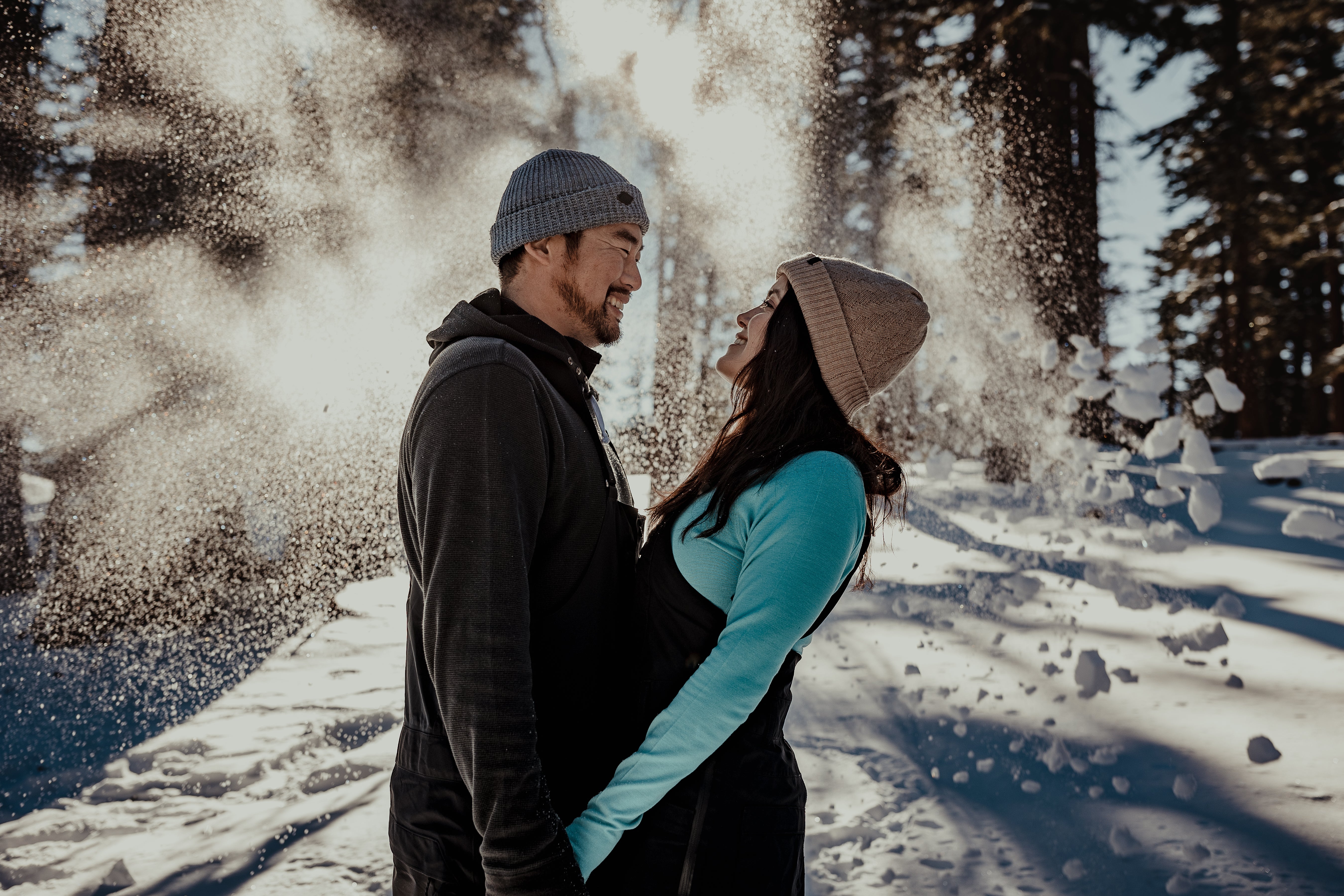 a couple wearing Ridge Merino winter layers smiles at each other while sun pours through the snowy trees in the background