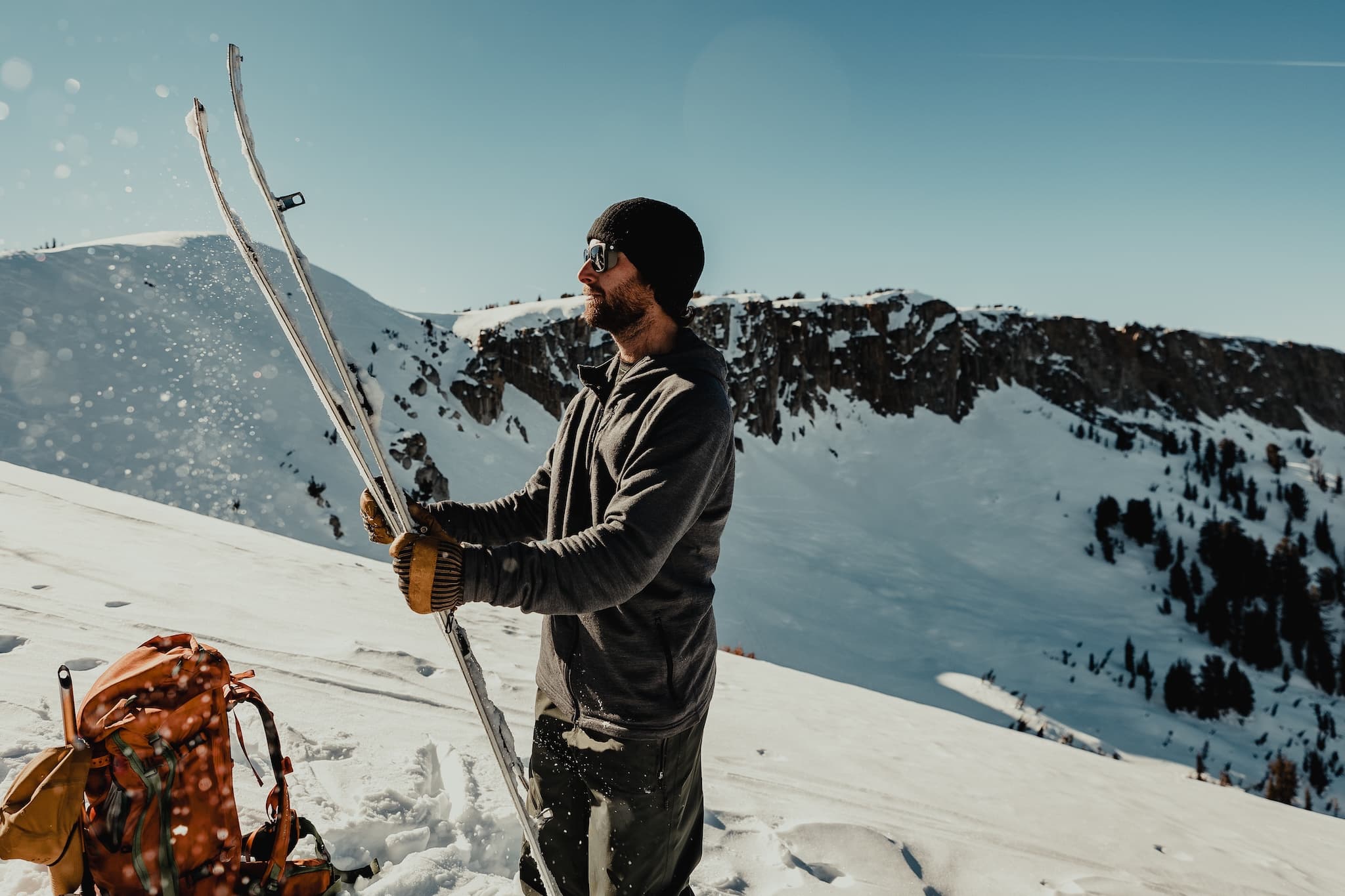 a backcountry skier wearing a Convict Canyon Hoodie knocks snow off his skis