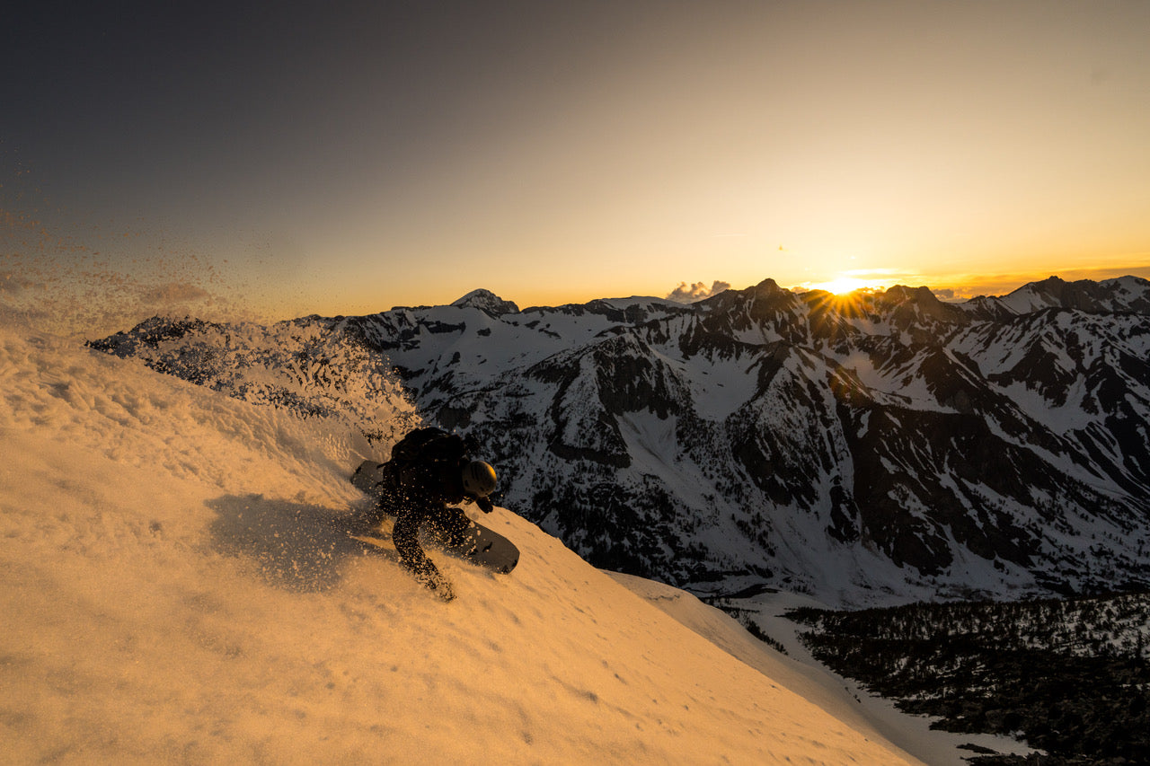 a snowboarder cruises down a run as the sun sets over the Eastern Sierra mountains