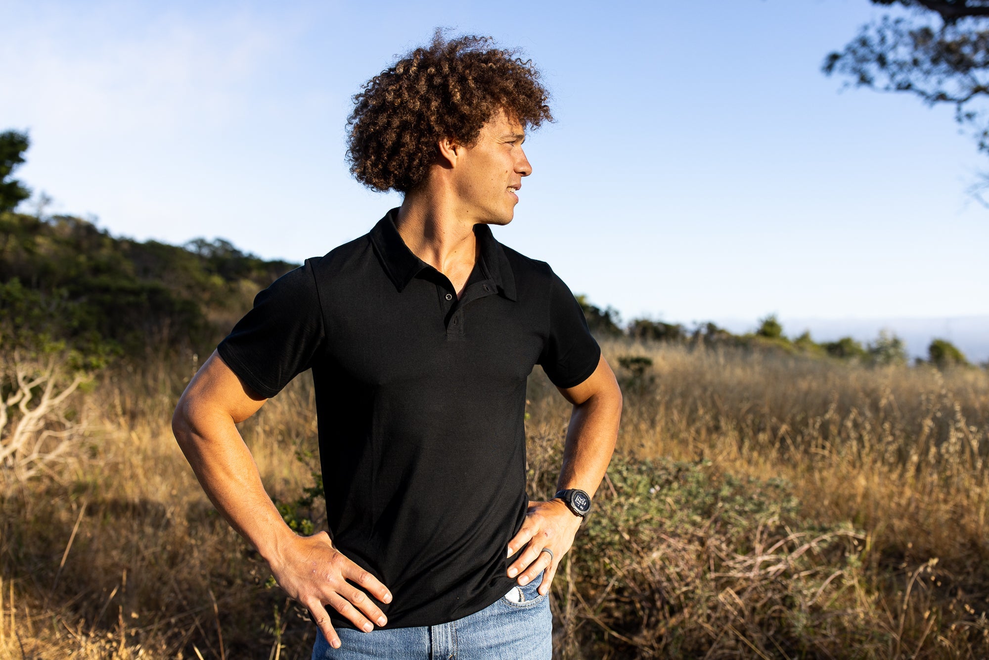 a man wearing a black Ridge Merino Journey Polo Tee in a field