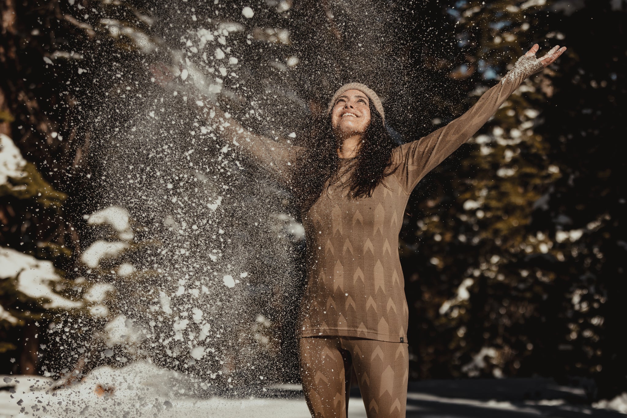 a woman wearing Ridge Merino layers throws snow in the air