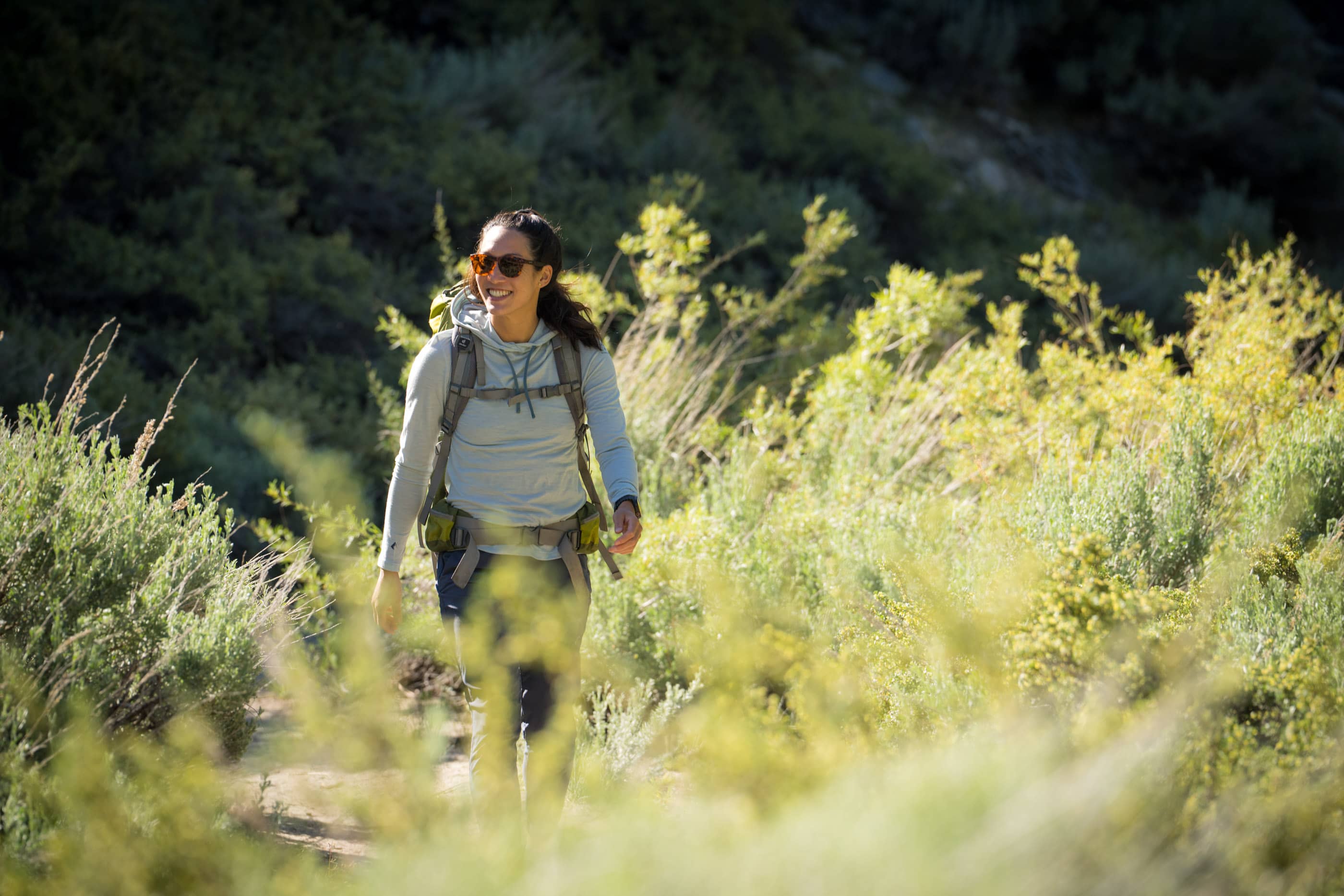 a woman smiles on a hike wearing a Solstice Sun Hoodie
