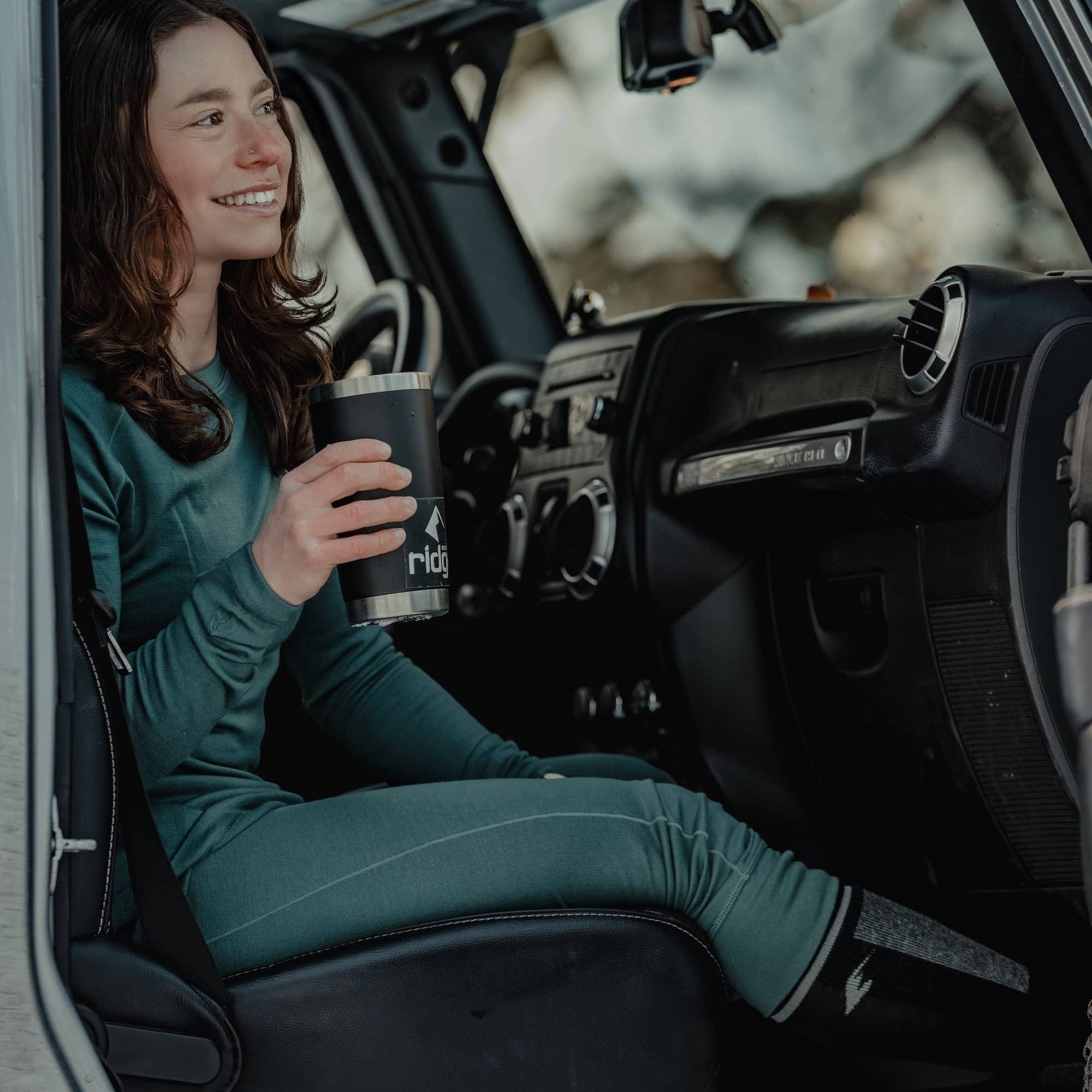 a woman sitting in a car wearing green Ridge Merino Inversion Base Layers