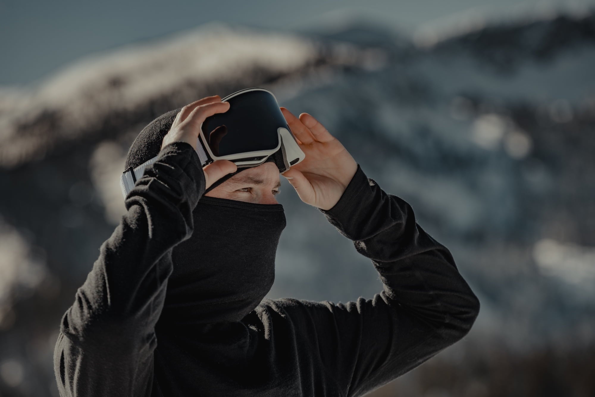 a man putting goggles on over an Aspect Balaclava Hood Base Layer Top