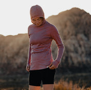 a woman wearing a Pursuit Ultralight Merino Hoodie in Wild Rose