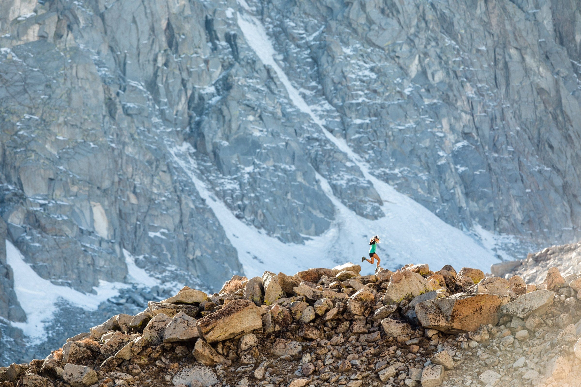 a runner wearing an Aspect long sleeve shirt runs a rocky trail beneath snowy mountains