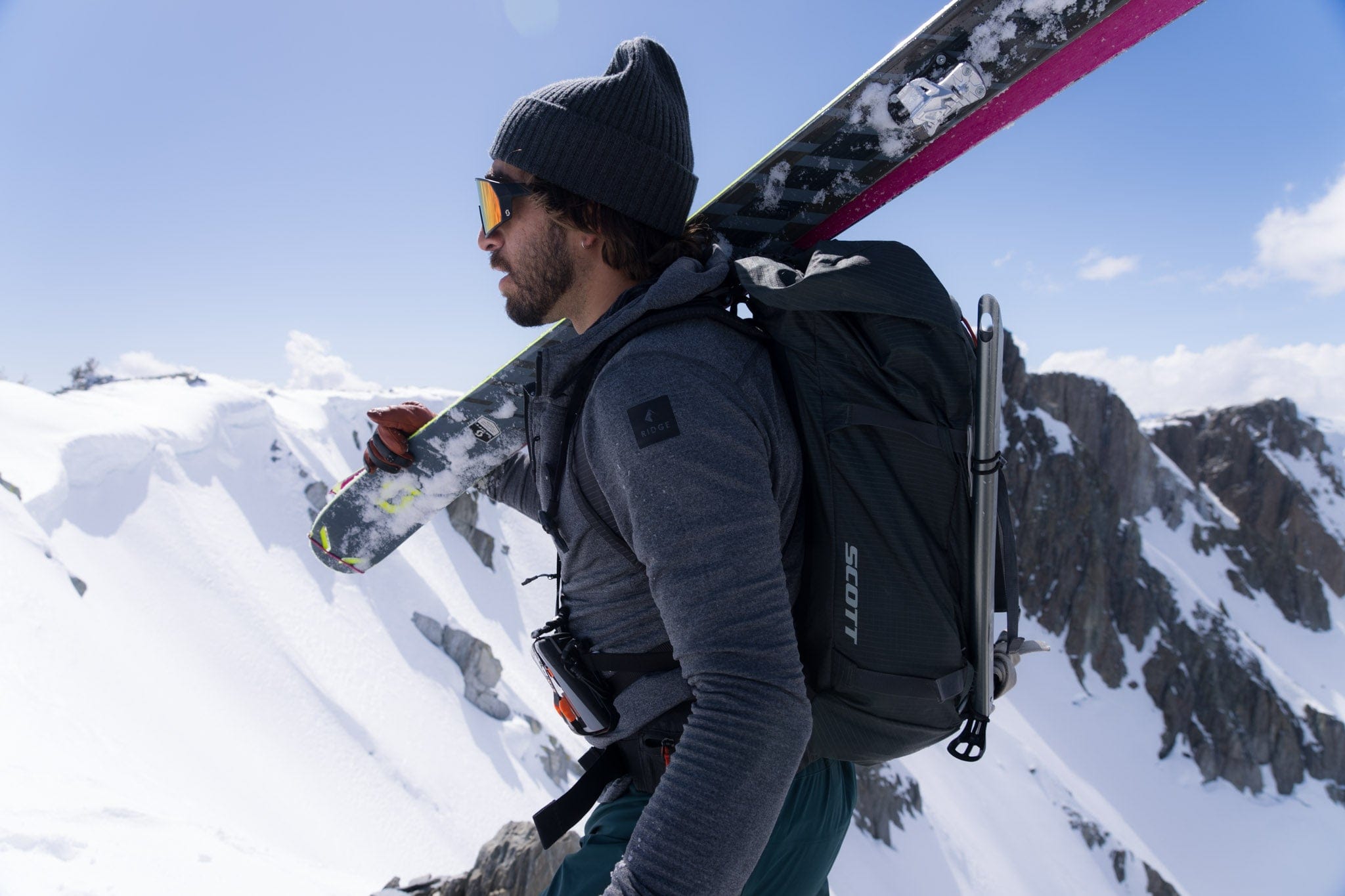 a backcountry skier carries his skis on a ridge line wearing a Ridge Merino Convict Canyon Hoodie