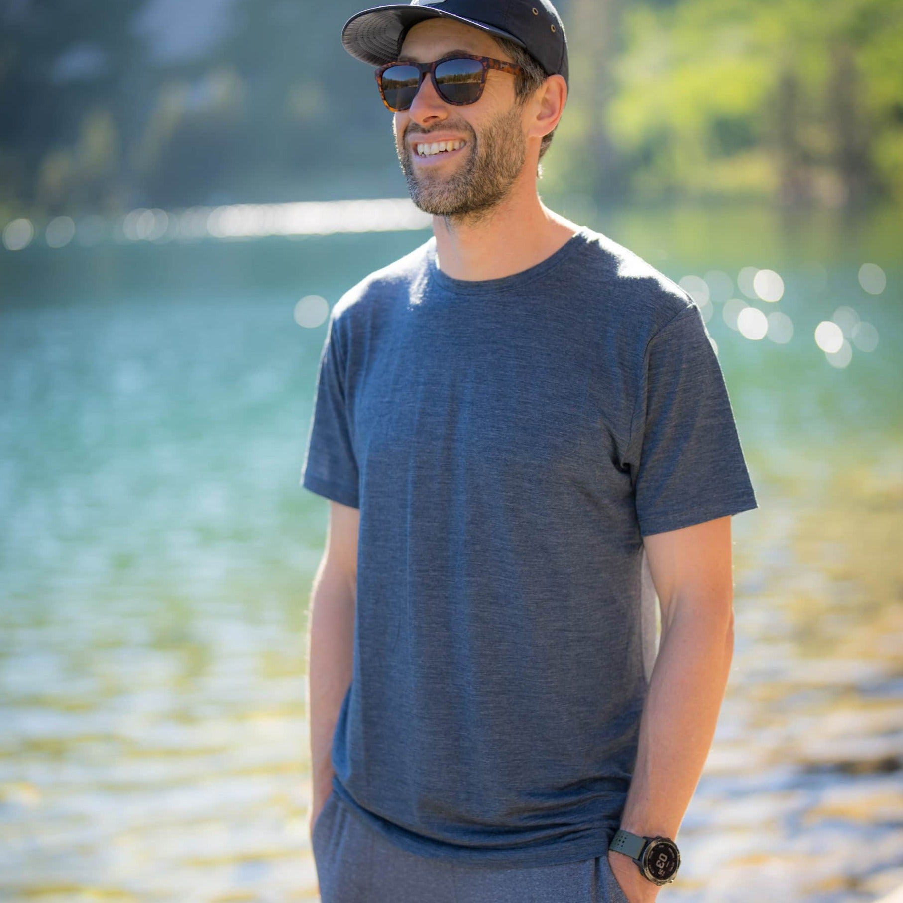 A man stands by a lake wearing the Ridge Natural Tee and a Ridge Merino hat