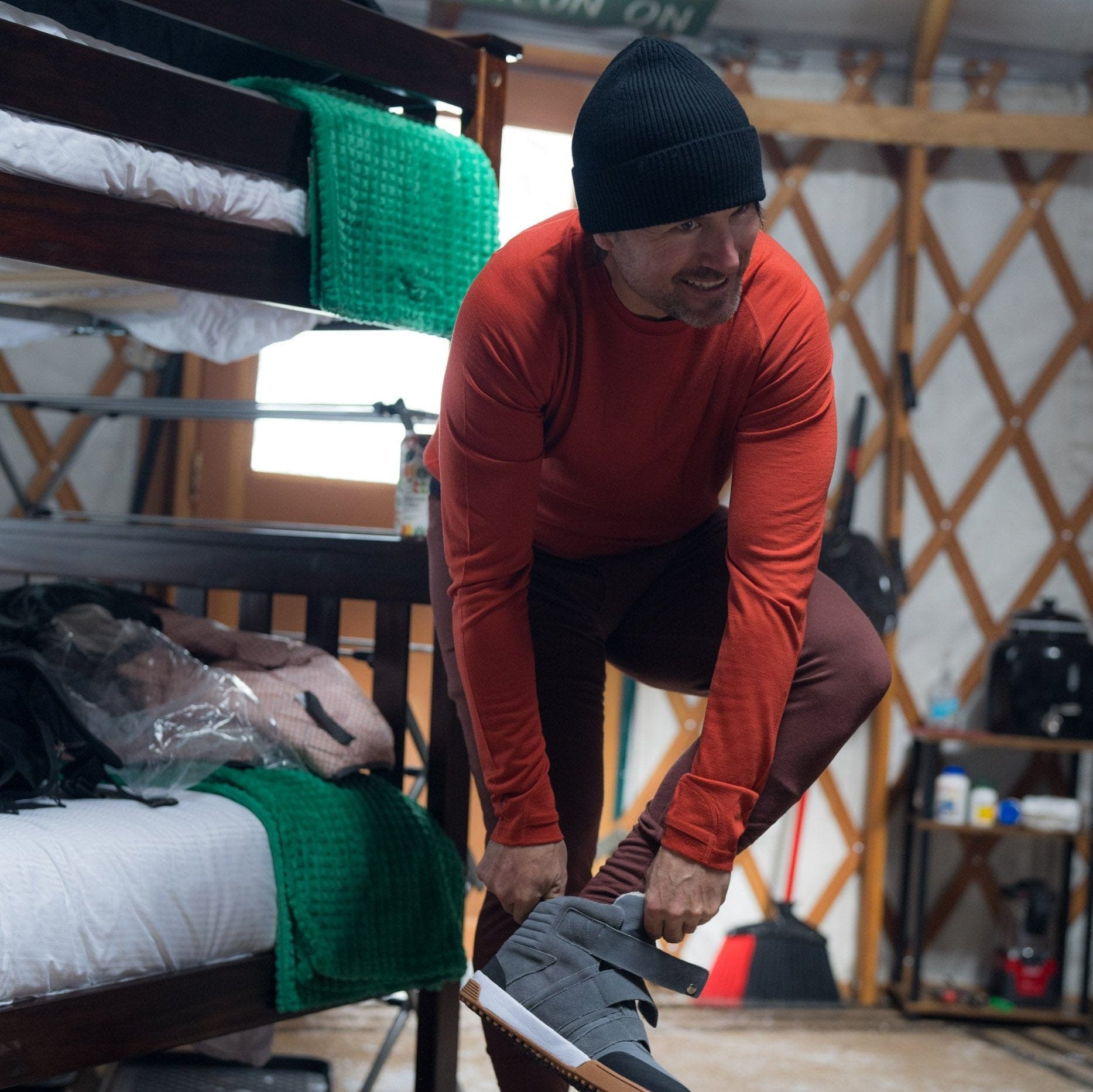 a man putting on shoes in a ski yurt wearing Inversion 100% Merino base layers